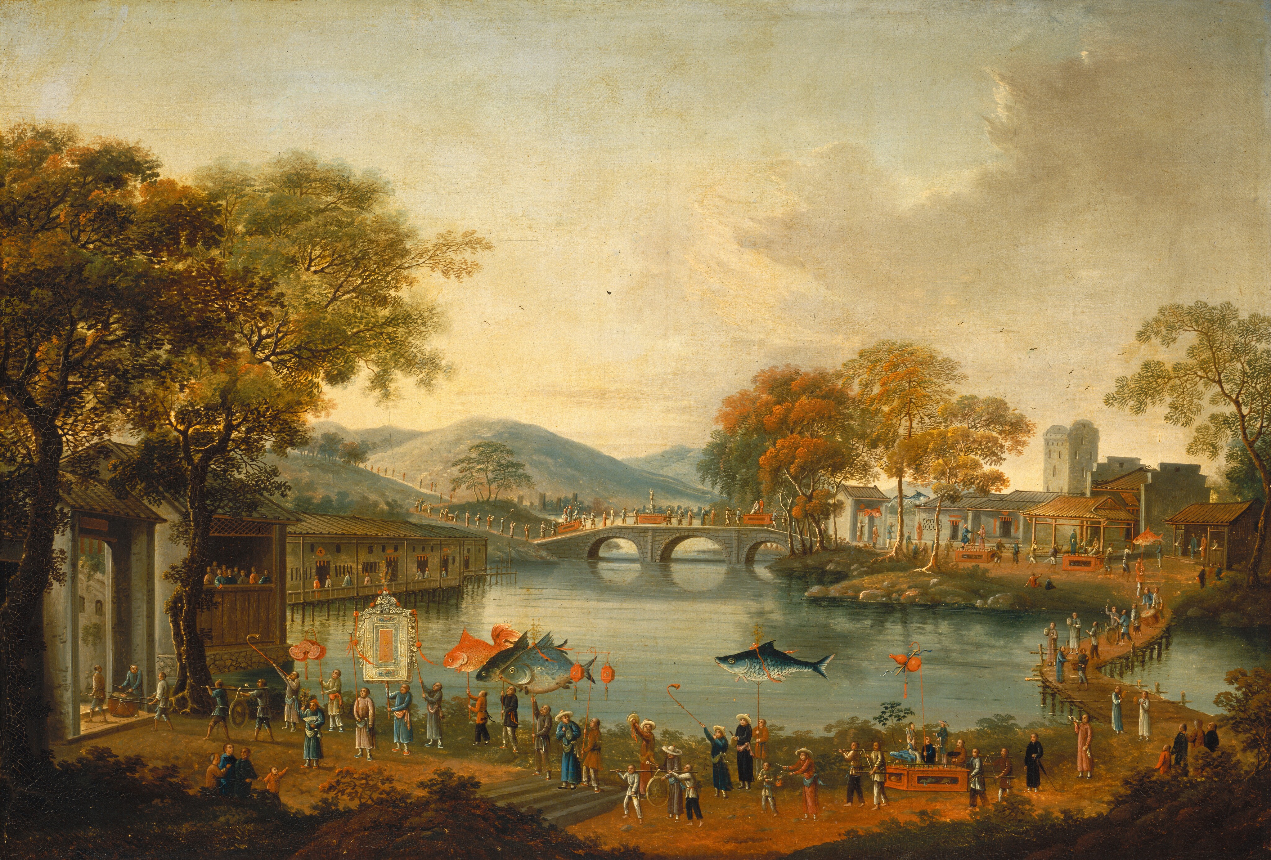 This painting shows a waterfront viewed from high above. In the background, light blue hills obscure the horizon line. In front of these hills, a stone bridge arches across the water, connecting two sides of a river. Another bridge crosses the river on the right side of the painting. At the bottom of the painting, an ornate procession with lanterns and banners in the shape of large fish takes place close by. Both adults and children are involved in the procession, and the line of people snakes back across the bridge at the right, across the stone bridge, and into the distant hills. On the opposite shore are small buildings with red-tiled roofs, and a tower stands prominently in the background. The procession ends in a large building in the bottom left corner of the image, framed by tall trees. The color palette features warm earth tones with shades of ochre and rust, contrasted by the soft greens of the trees and the blues and grays of the water.