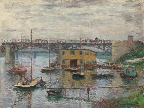 We look across a glimmering river toward docks, about a dozen small boats, and a mustard-brown, boxy building under a bridge that crosses the width of the canvas in this horizontal landscape painting. A patch of green grass lines the riverbank in the lower right corner of the canvas. The land curves away out of sight, and then back into the scene below the abutment of the bridge along the right side of the painting. From the ivory-colored abutment, the straight deck of the bridge is supported by two shallow, iron-gray arches, and the bridge extends off the left side of the composition. Dots of red and gray on the bridge suggest vehicles or pedestrians. The river below is painted with blended strokes of silvery gray, icy blue, and pale lavender purple around the low-sided sailboats. One turquoise-colored houseboat is pulled up to the riverbank to our right. The long, rectangular, flat-topped building is pierced with two stories of windows, which are outlined in spruce green against the golden yellow. The horizon line runs just below the bridge deck, just under halfway up the composition. The sky above is painted with longer swipes of cream white and smoke gray. Loose, short brushstrokes are visible throughout, especially in the water, boats, and bridge. The artist signed the painting in the lower right corner, "Claude Monet."