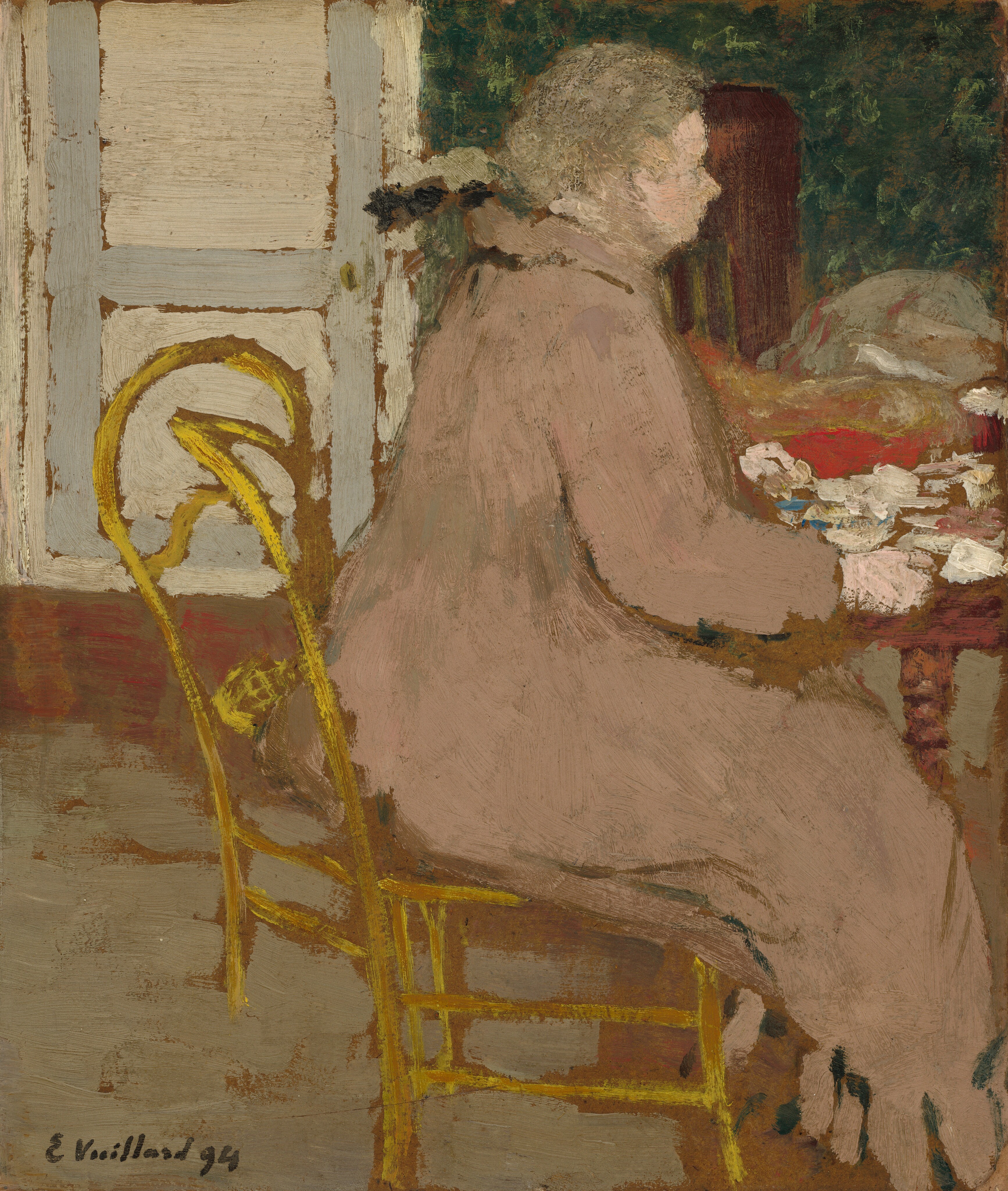 This painting shows a person seated at a table in a bright yellow chair, facing the right. The person has pale skin and gray hair, and they are wearing a loose-fitting light brown garment, similar to a long coat or dress. On the table in front of them appear to be various indistinct objects in shades of white and red. The background has a dark green area on the right which may be a wall or curtain, with a lighter area on the left that maybe be a window or door. The floor is painted in shades of brown and beige. The brushstrokes in the painting are thick and visible, making the scene appear blurred.