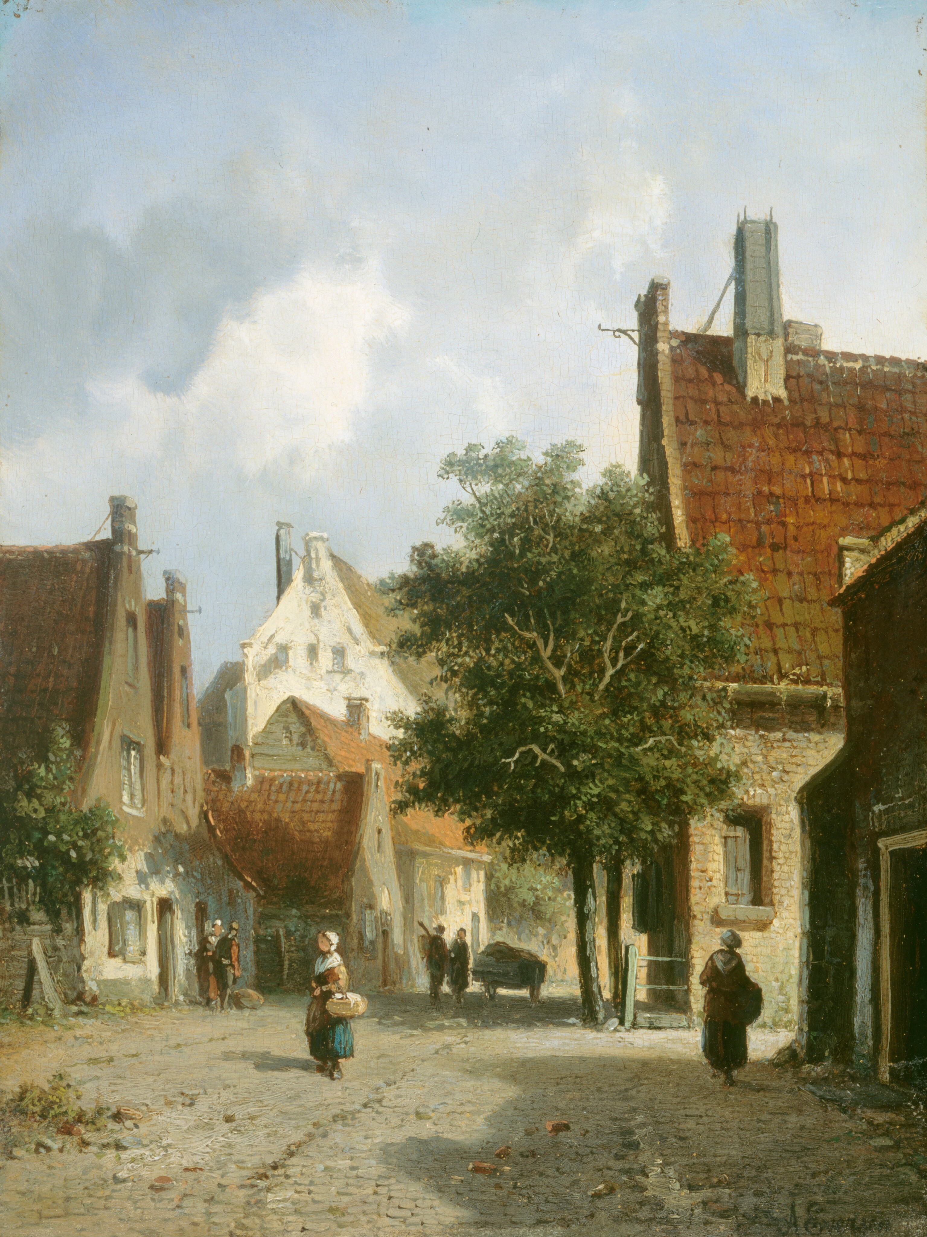 This painting shows a cobblestone street lined on both sides by buildings and tall green trees. A building with a red-tiled roof and stone walls is visible on the right, partly covered by tree branches. On the left are more buildings with red roofs and white walls, some shorter and some taller. People walk along the stone street. Closest to us, two women are visible carrying baskets, both wearing long dresses or skirts in shades of red and blue with white bonnets covering their hair. In the background, farther down the road, two men stand next to a cart, and two people on the left stand near the entrance to one of the buildings. The sky above is cool blue with a few clouds, and the scene is lit with a warm light. The buildings and trees on the right side of the street cast dark shadows.