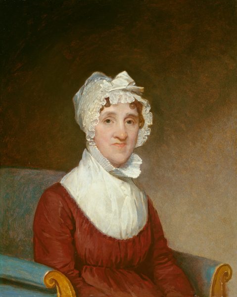 This painting shows the upper body of a woman seated in a chair. She is wearing a white bonnet with ruffled edges, covering her wavy, light brown hair. Her facial features include fair skin, thin lips, a long nose, and a pointed chin. She is dressed in a deep red gown with a high white collar. The chair has a blue cushion and wooden frame with curved armrests. The background is a gradient of brown at the top and tan at the bottom.