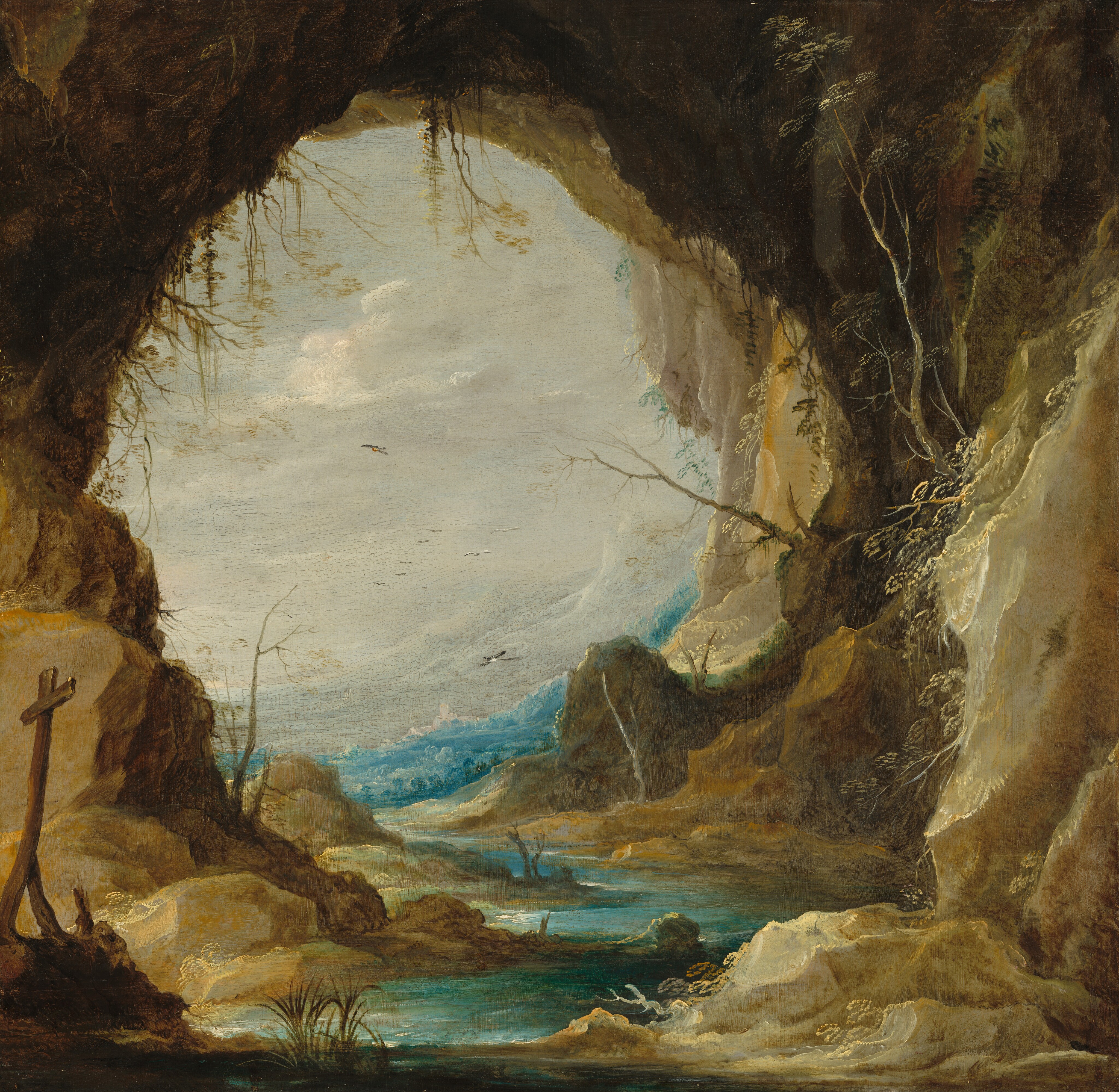 The round, cavernous entryway of a craggy grotto that opens onto vivid blue water nearly fills this square landscape painting. Close to us, steep, tan-colored and earthy brown rocks rise like cliffs to each side. A wood cross set on a low rocky outcrop lists to one side in the lower left corner of the composition.  A few tufts of grass or reedy plants are interspersed along the winding path of the turquoise-colored water inside the grotto, and more spindly plants grow up from or out of the rocky surfaces. The waterway zigzags between us and the body of water just beyond the opening. White highlights suggest white caps or surging waves. A band of opal-white mountains follow the curve of the grotto opening to angles up to the right. They nearly blend into the pearly white sky and the screen of clouds there. Black and white birds fly in the distance. One is near the water on the far side of the grotto opening, and one is higher and farther back. At least seven are tiny in the deep distance.