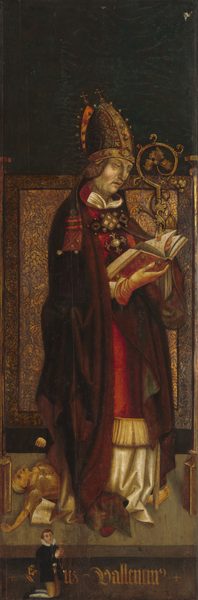 The image shows a man dressed in ornate, ecclesiastical attire, standing with his body slightly turned to the side, reading from a book. His facial features are European with delicate eyes, and his hair is medium brown, curling slightly beneath a detailed mitre adorned with crosses. He wears a richly decorated robe of deep red and gold, with white garments visible at the collar and hem, and a large brooch on his chest. A tall, ornate crozier is beside him, designed with gold-colored metalwork. At the bottom of the image, a small figure kneels in prayer, wearing black clothing with a ruffled collar and holding a red rosary. Another smaller figure is partially visible at the feet of the main subject. The background features a dark tapestry-like texture.