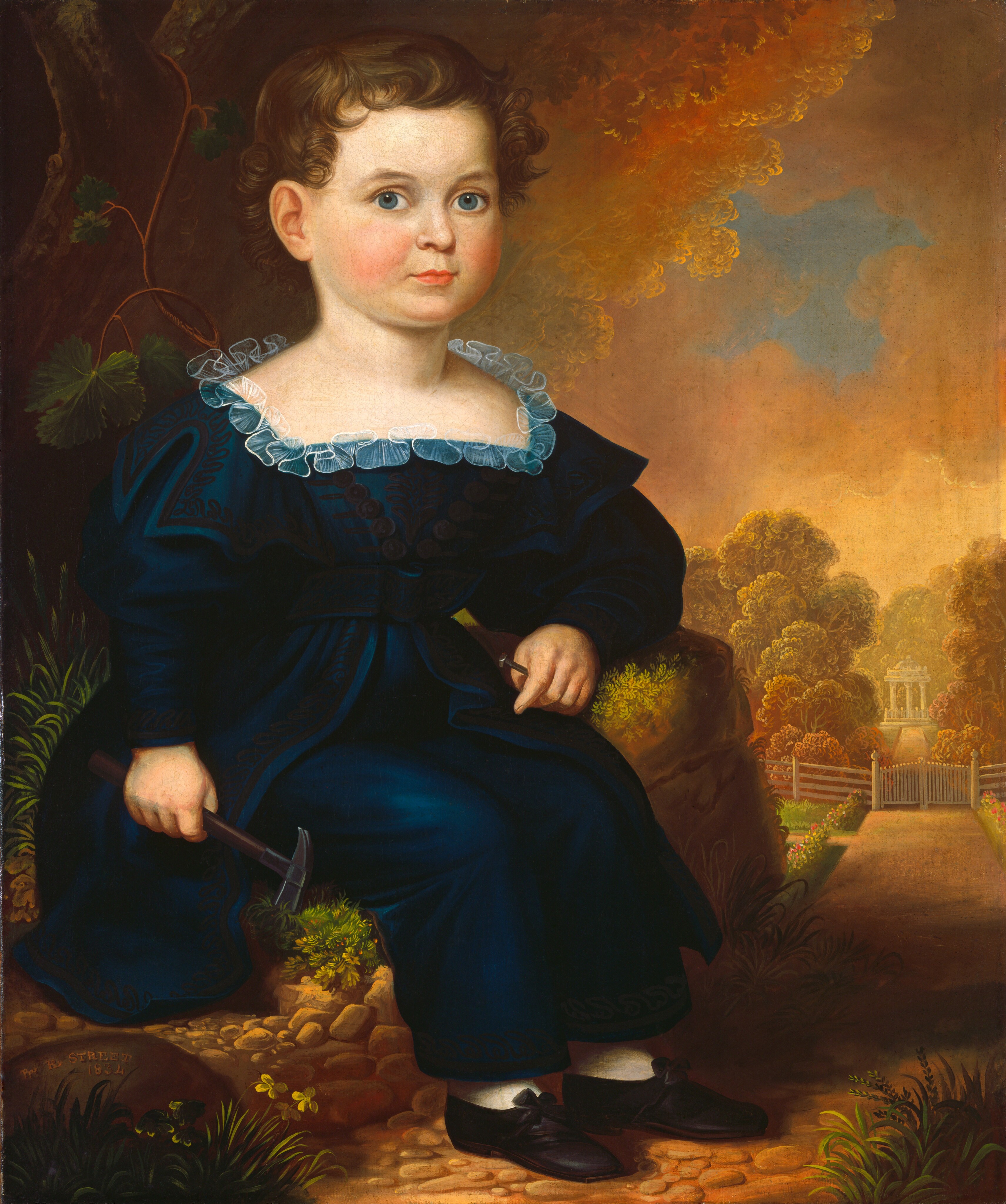 The image shows a young child seated on a rock in a garden setting. The child has fair skin, rosy cheeks, large blue eyes, and curly brown hair. They wear a dark blue dress with a lace collar, and dark shoes with bows over white socks. The child holds a small hammer in their left hand. The background features lush greenery, a stone path, a small, white gazebo, and a picket fence with flowers.