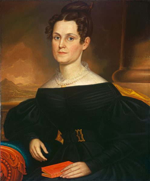 The image shows a woman seated in an ornate armchair. She has fair skin, blue eyes, dark hair styled in an updo, and is wearing a dark dress with puffed sleeves and a lace collar. She holds a red book and there is a double-strand pearl necklace around her neck. In the background, there is a column and a landscape with mountains under a cloudy sky.