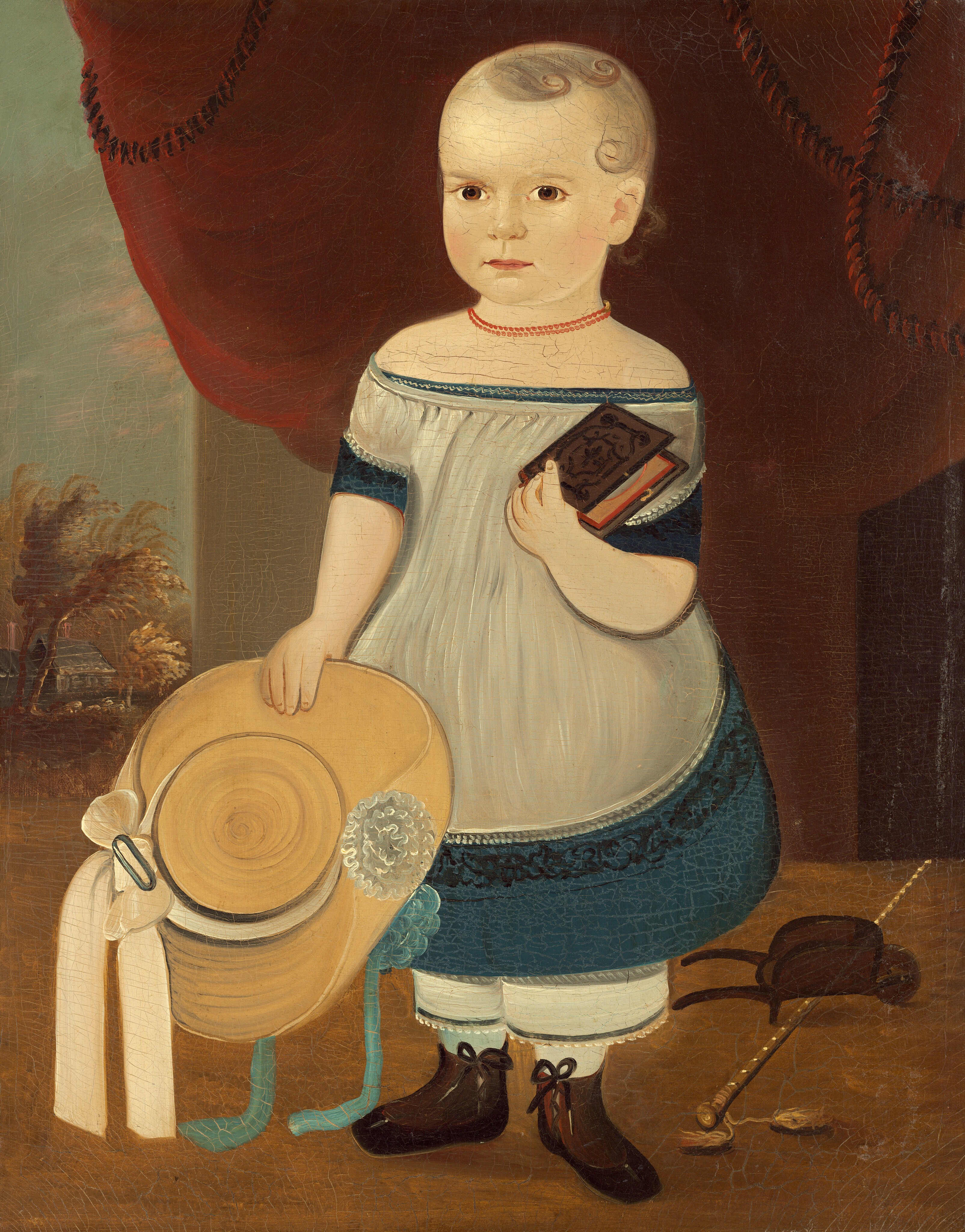 The image shows a young child standing. The child has a light complexion, rosy cheeks, and blonde hair styled in short curls. They are wearing a white dress with blue trim, boots with tied laces, and hold a book in their right hand and a straw hat in their left hand. They wear a red bead necklace and next to them are a cap and a walking stick with tassels. In the background, there is a red curtain at the top, with trees and a building visible on the left side.