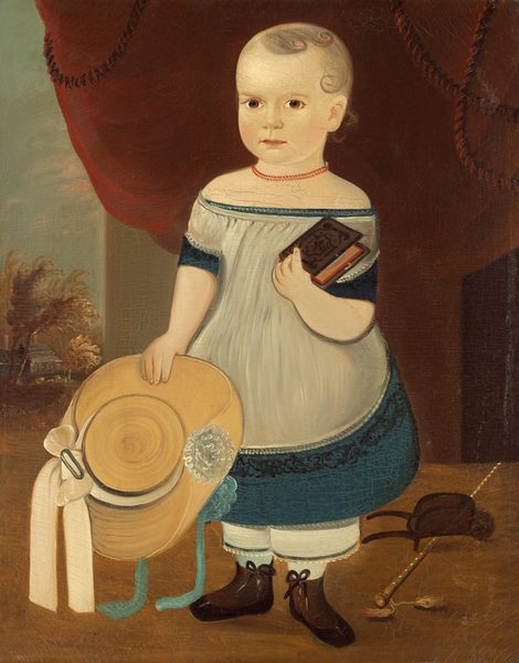 The image shows a young child standing. The child has a light complexion, rosy cheeks, and blonde hair styled in short curls. They are wearing a white dress with blue trim, boots with tied laces, and hold a book in their right hand and a straw hat in their left hand. They wear a red bead necklace and next to them are a cap and a walking stick with tassels. In the background, there is a red curtain at the top, with trees and a building visible on the left side.