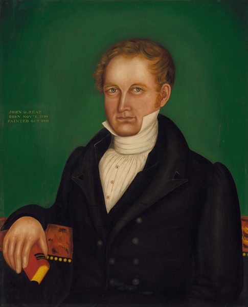 The image shows a man with fair complexion and light brown hair, depicted in a half-length portrait. He is seated, facing forward with a slight tilt to his left. The man has sharp eyebrows, deep-set eyes, a defined nose, and lips, creating a composed expression. He is dressed in a formal black coat over a white shirt with intricate ruffles, and holds a red book in his right hand. A red and gold textile is draped over the armrest of his chair. The background is solid green. Text on the left side of the image states "JOHN G. READ BORN NOV' 1, 1799 PAINTED OCT' 1833."