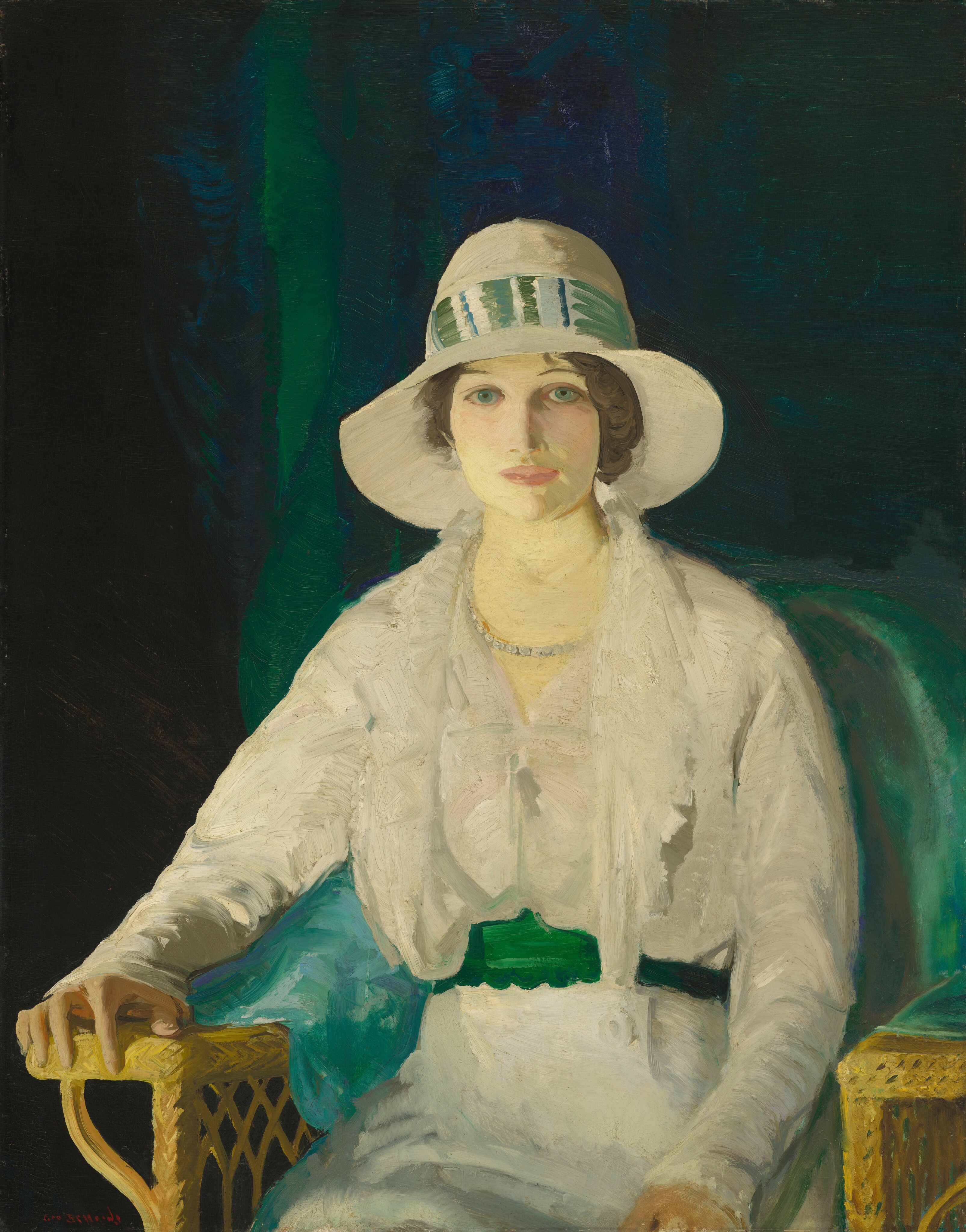 This painting is a portrait of a seated woman shown from the knees upwards. She is seated in a woven yellow armchair, with her right arm resting on one arm of the chair, while her left hand rests on her lap. The chair is slightly turned to the left, but she looks directly at us. She has pale skin with slightly pink cheeks, round blue-green eyes, thin brown eyebrows, and pink lips set in a neutral expression. Her hair is dark brown and styled in soft waves, visible beneath a wide-brimmed cream hat adorned with a striped green-and-white band. The woman wears a white dress with a green belt or sash around the waist and a pearl necklace. A green cloth appears to be draped on the chair beneath her, and the background is a deep blend of green, dark blue, and black shades, similar to a heavy draped curtain. The brushstrokes in the painting are thick and visible.