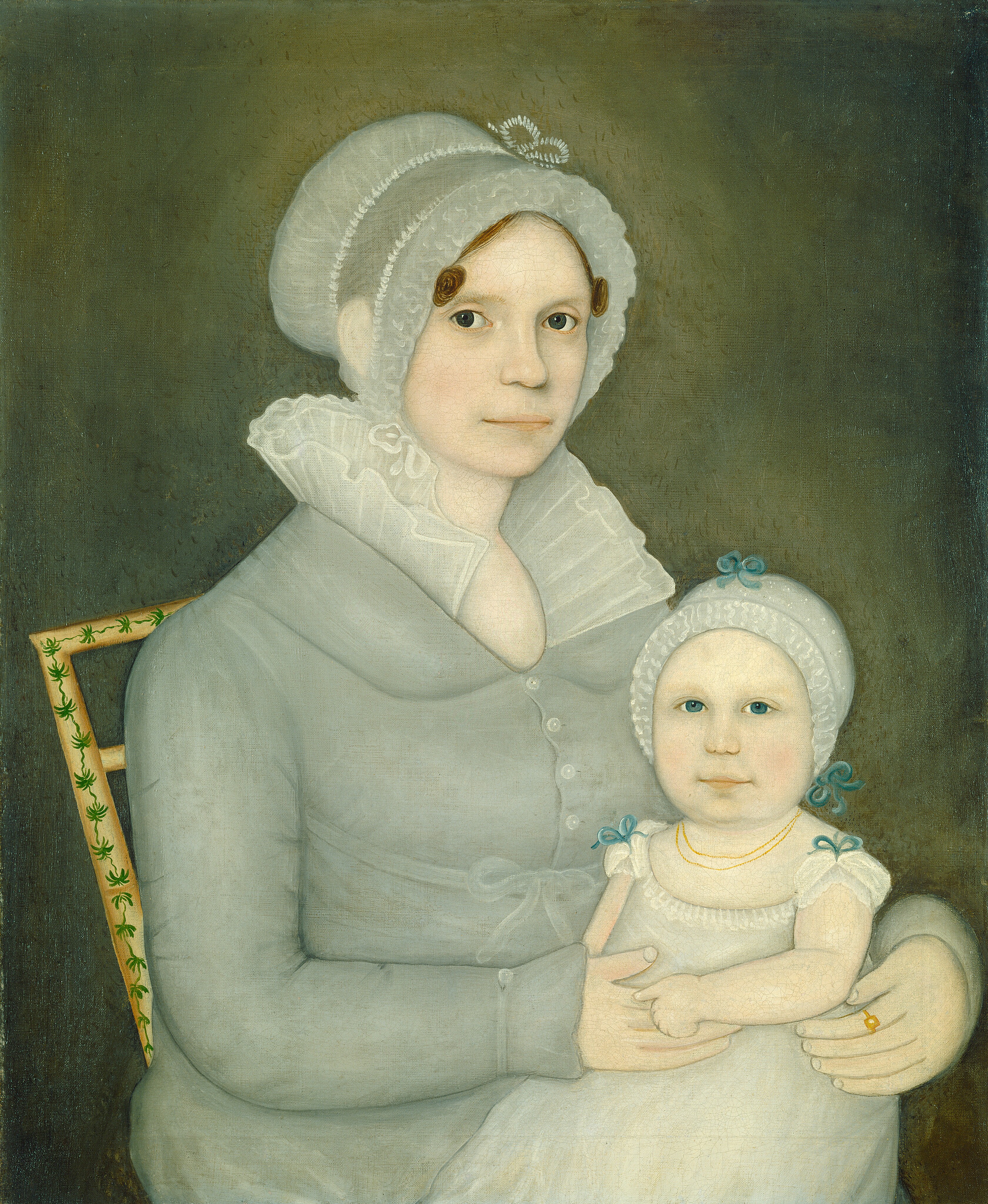 The image depicts a woman seated with an infant on her lap. The woman is facing slightly to the left with her head turned towards the viewer. She has a calm expression with large eyes, thin lips, and dark hair under a lace-trimmed cap. She wears a high-collared dress with buttons and a shawl around her shoulders. The infant gazes directly at the viewer, wearing a bonnet with light blue ribbons and a white dress with a gold necklace. The woman's hand rests on the child, with a gold ring on her finger. The background is a dark, textured tone with a decorative chair featuring green, leaf-like designs.