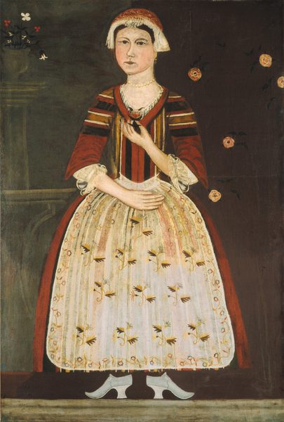 The image shows a woman in a full-length portrait. She has a pale complexion, arched eyebrows, a small mouth, and dark eyes. She wears a cap, a red and gold dress with white lace detailing, and floral patterns. Her shoes are visible beneath the dress, and she wears a pearl necklace. She holds a dark object in one hand and has the other hand on her waist. The background is dark with flowers on the left and a pattern of roses on the right.