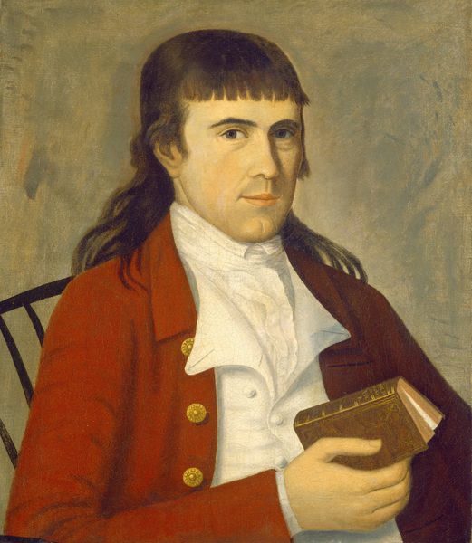 The image shows a man from the waist up, sitting with his body slightly facing left and his head turned towards the viewer. He has a long face, defined features, fair complexion, and dark hair framing his face and extending to his shoulders with a straight fringe across his forehead. He is wearing a red coat with gold buttons over a white high-collared shirt, holding a closed book in his right hand. The background is plain with earthy tones and a subtle texture, emphasizing the figure. A dark chair is partially visible behind him on the left side of the image.