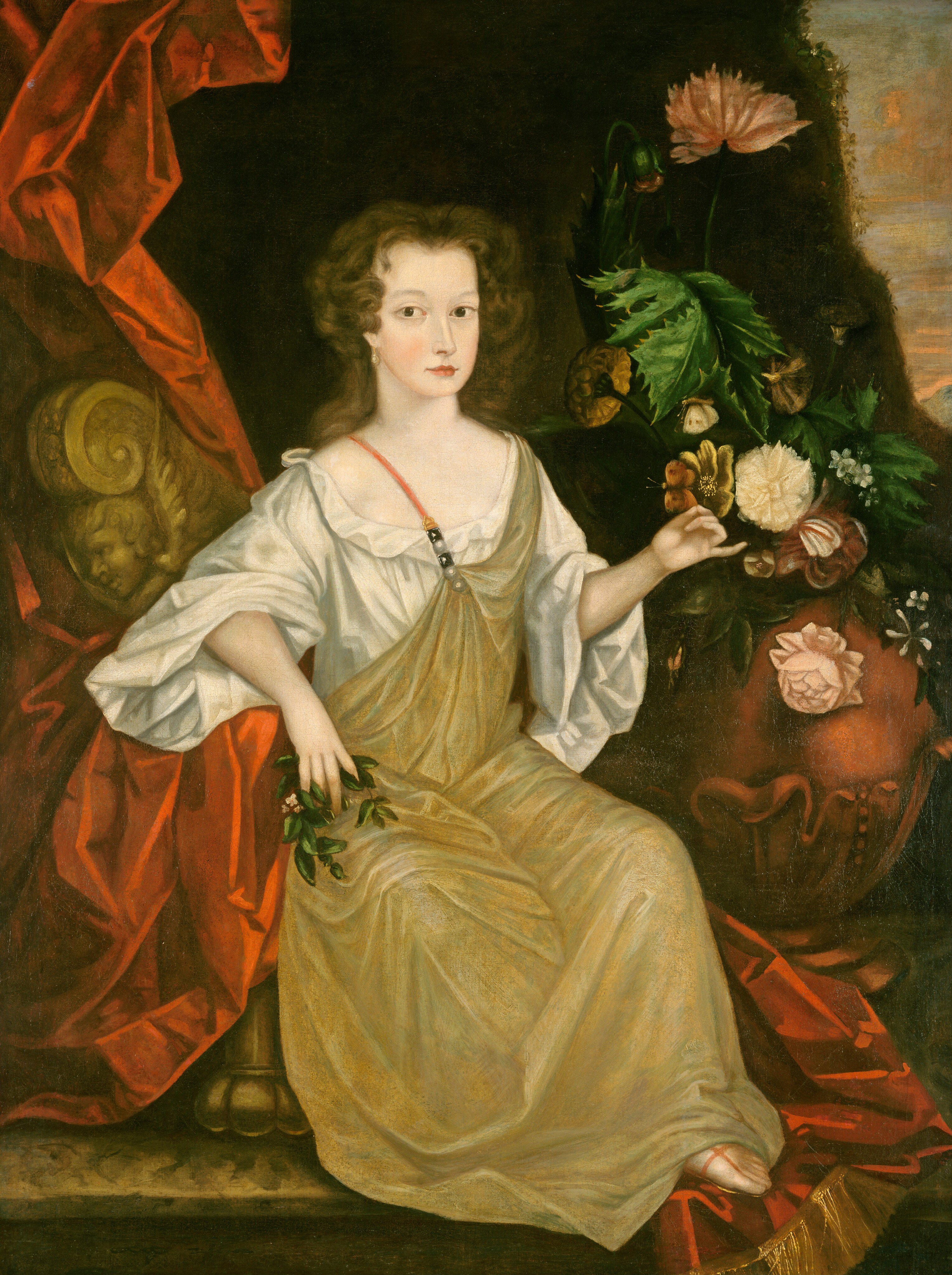 This painting shows a young woman seated on an ornate yellow-brown chair, with her body slightly turned to the left and her head facing us. She has fair skin, dark wavy hair, a long nose, pale eyebrows, and small red lips that are slightly turned up at the ends. She is wearing a white gown with wide sleeves and a light greenish-yellow cloth draped over her shoulder and legs, perhaps a smock or apron, secured over her other shoulder by a beaded strap. She is holding a small sprig of greenery in her right hand, which rests on an arm of the chair, and her left hand is outstretched towards a round red vase on the right of the painting filled with flowers in shades of pink, cream, and pale yellow, with large green leaves. Two butterflies float above her hand in shades of cream and pale red. Her feet are visible below the hem of her dress, resting on the ground near the bottom right corner. The background features a dark red draped curtain that comes down from the top left corner and appears to cover most of the chair she sits on. The wall behind her and the colorful flowers is dark, with one section in the top right corner appearing to show a sliver of light blue sky with pink clouds.