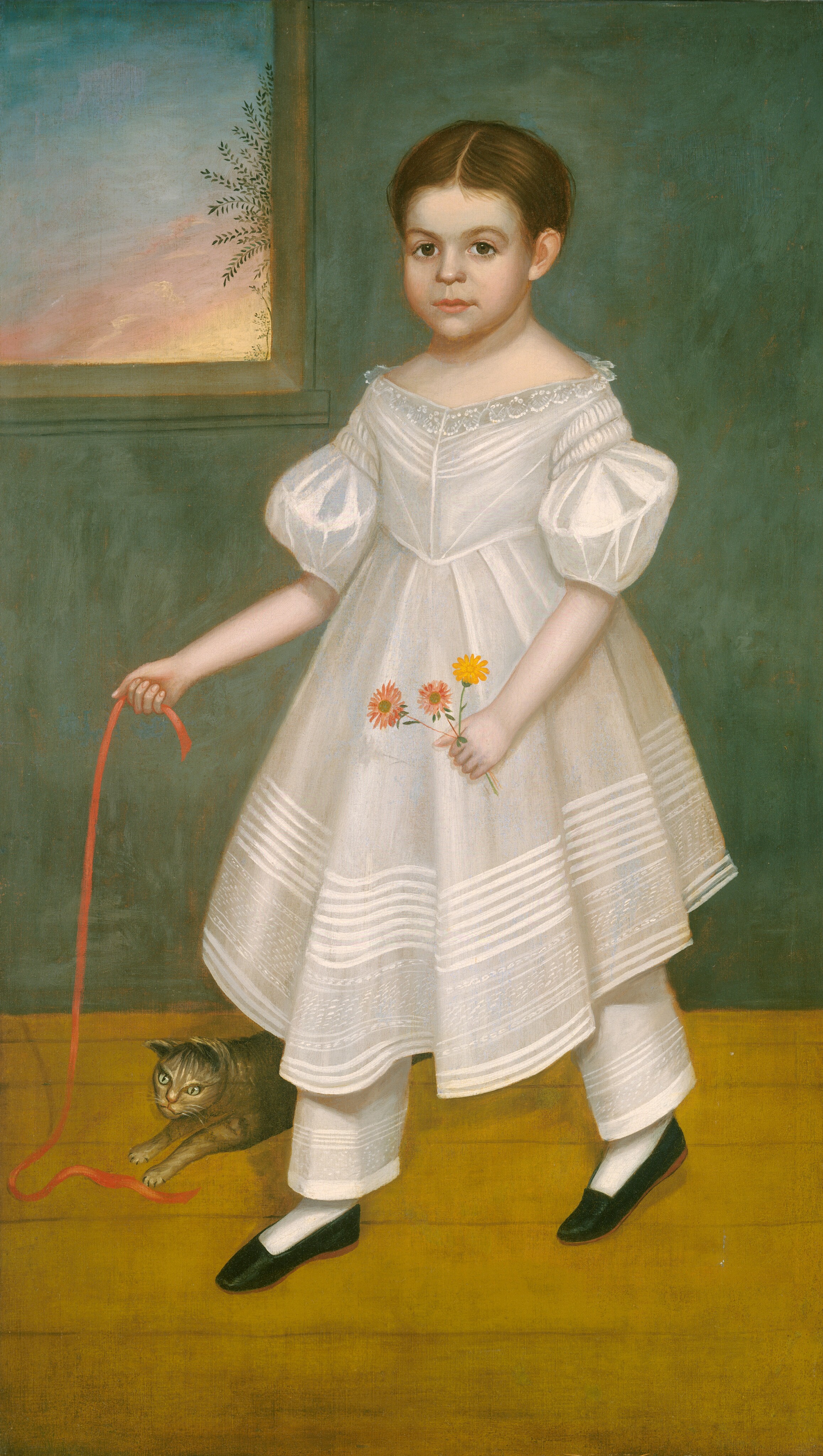 The image shows a full-body portrait of a young child standing indoors. The child faces forward with a neutral expression, looking directly at the viewer. They have neatly styled brown hair parted in the middle. The child wears a white dress with lace detailing at the collar and puffed short sleeves, over layered pantaloons. The dress has intricate patterns along the hem. They hold a bunch of flowers in their left hand and a red ribbon in their right hand, which trails down to the floor. A small cat playfully touches the end of the ribbon near the child's feet. The child wears white socks and black shoes. The background consists of a green-tinted wall and wooden floor, with a window on the left showing a glimpse of the sky with foliage and a warm sunset hue.
