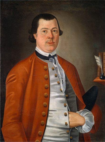 The image shows a man from the waist up, facing slightly to the right. His fair complexion contrasts with short, dark brown hair that curls a little at the ends. He maintains direct eye contact with a neutral expression, and has distinct rounded cheeks. He wears formal attire with a white shirt, buttoned waistcoat, and deep orange overcoat with gold buttons. He sports a white cravat, elaborate ruffled cuffs, and his right hand is in his waistcoat. In the background, to the right, there is a shelf holding objects like a bound book and a quill in an inkwell. The backdrop is plain and brown.