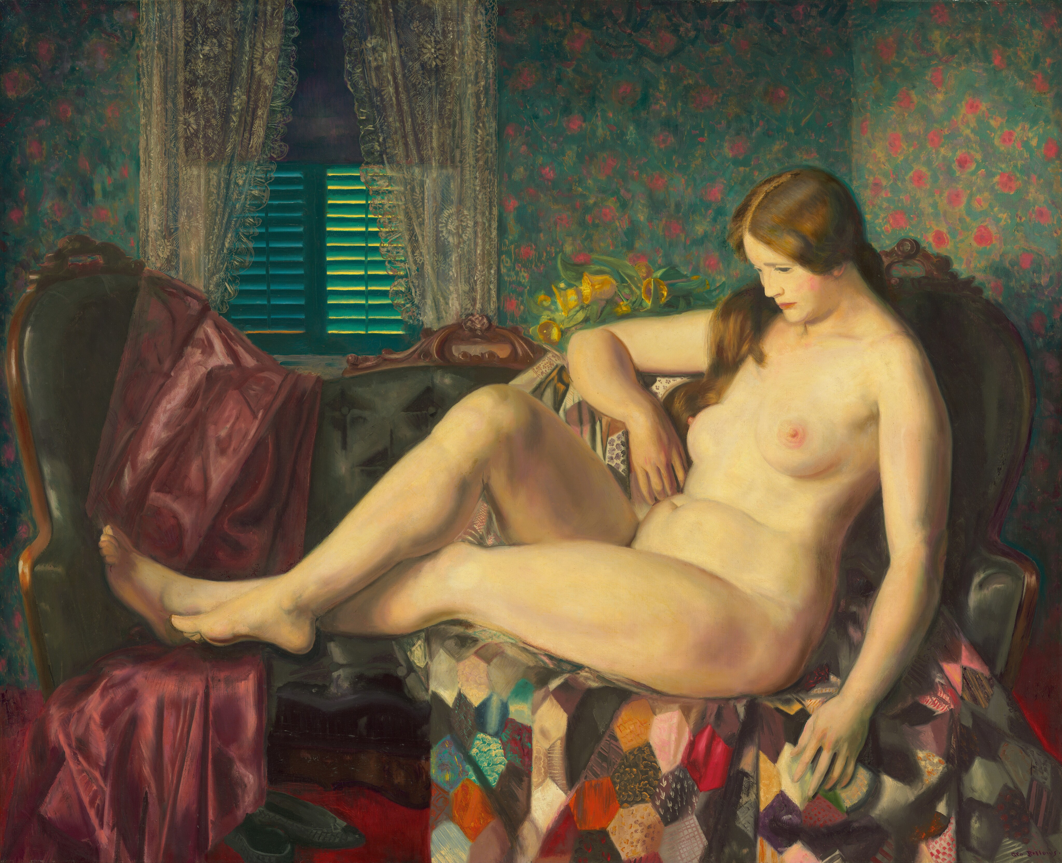 This painting shows a reclining nude female figure on an upholstered couch. She is turned to the side, with her crossed legs extending to the left and one arm resting along the top of the couch. She has pale skin and long chestnut brown hair that cascades over her shoulder. She is looking downward at her own legs and sits atop a colorful patchwork quilt. The couch is a teal color but is covered by the quilt and another soft red blanket or cloth. The room behind the couch has blue floral wallpaper, lace curtains, a closed window with green shutters, and a vase with yellow flowers on a nearby surface.