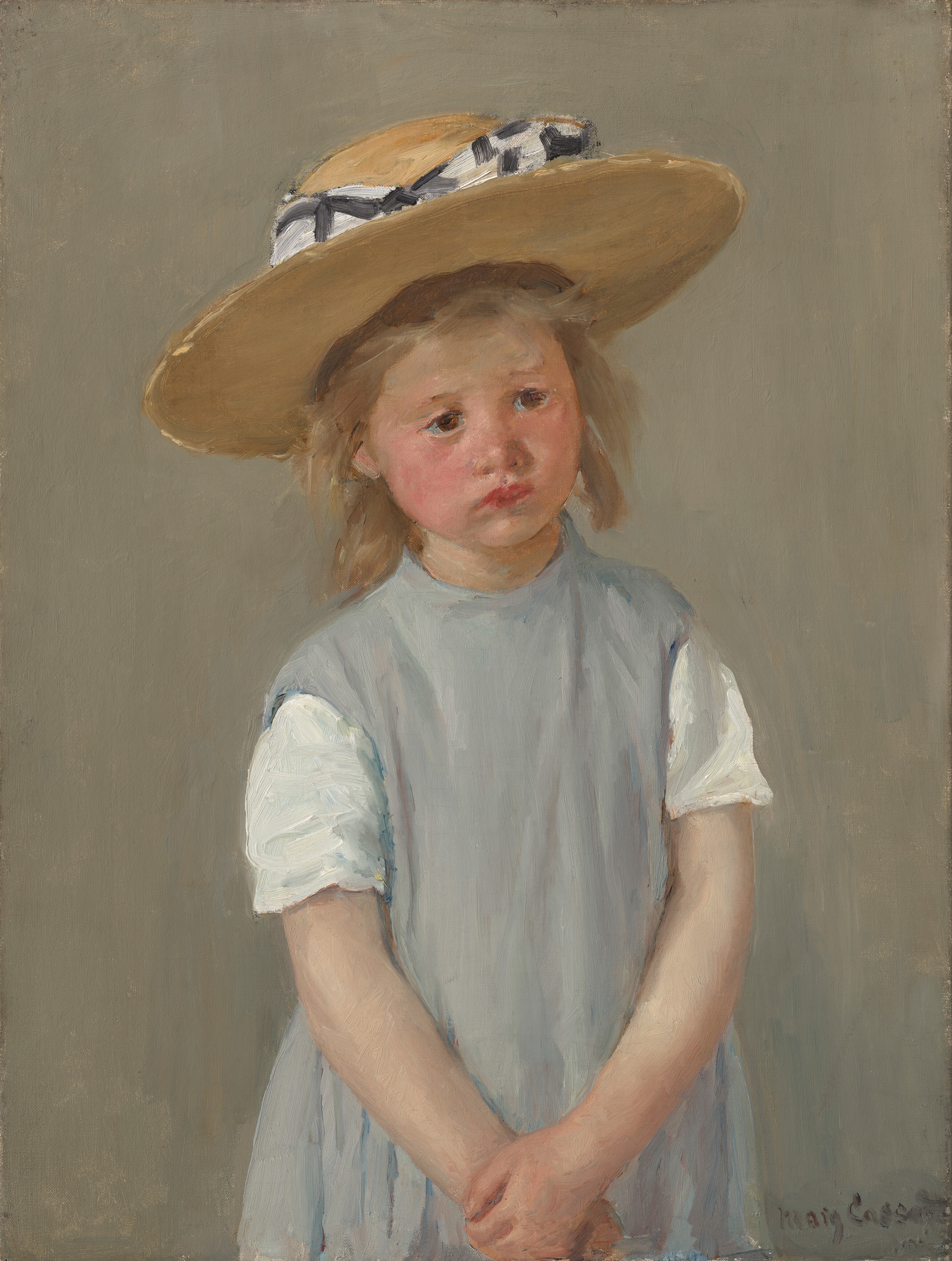 Shown from the waist up, a young girl wearing a slate-gray dress and straw hat stands with her hands clasped in front of her in this vertical portrait painting. The girl has light, peachy skin, and her cheeks are lightly flushed. Her body faces us but she tips her head slightly to her right, our left, and looks off into the distance with dark brown eyes. Her faint eyebrows drawn together, and her cherry-red, full lips slightly turn down at the corners. She has a button nose and a rounded chin line. She has dark blond, straight, shoulder-length hair under a wide, flat-brimmed straw hat. The hat is wrapped around the crown with a checkered white and black bow. Her shoulders slope down as she holds one wrist with the other hand down in front of her. She wears a jumper over a shirt with short white sleeves. At first glance the jumper appears pale gray but closer inspection reveals strokes of pale lilac, ivory white, and cobalt blue. The girl’s features and clothing are painted with loose, visible brushstrokes, and the background behind her is painted with vertical strokes of tan blended with faint green. Short dabs of brighter gold and butter yellow give the impression of sunshine on the brim of the hat and in the girl’s hair. The artist signed the work with loose letters in the lower right corner, “Mary Cassatt.”