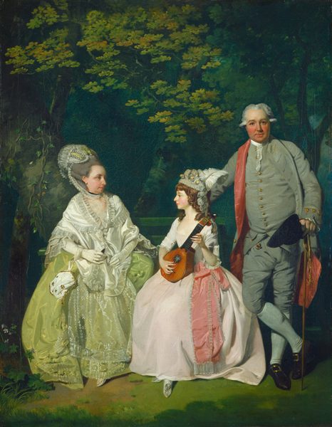 In this painting, three people are depicted in an outdoor setting. On the left, a woman stands or sits, looking to the right at the young girl next to her. The woman has pale skin, a long nose, and red lips, and her gray hair is in a large updo, styled with white lace and green ruffles. She wears a light green dress with lace details and a white ruffled shawl, with a white purse with gold details hanging from her wrist. In the center, the young woman also seems to be seated, looking to the left at the woman next to her. She holds a lute-like instrument in her lap. She has pale skin, and her brown hair is styled with curls and adorned with white feathers and small yellow flowers. She wears a pink dress with white sleeves and a darker pink sash. Behind her on the right, a man stands looking out at us, smiling slightly, holding a black hat and cane in his left hand. He is wearing a grey suit and a gray jacket with a red interior. His skin is slightly darker, with rosy cheeks and gray hair styled in tight curls above his ears. His right hand is behind the seated girl, and his legs are crossed. The background features layers of green foliage.
