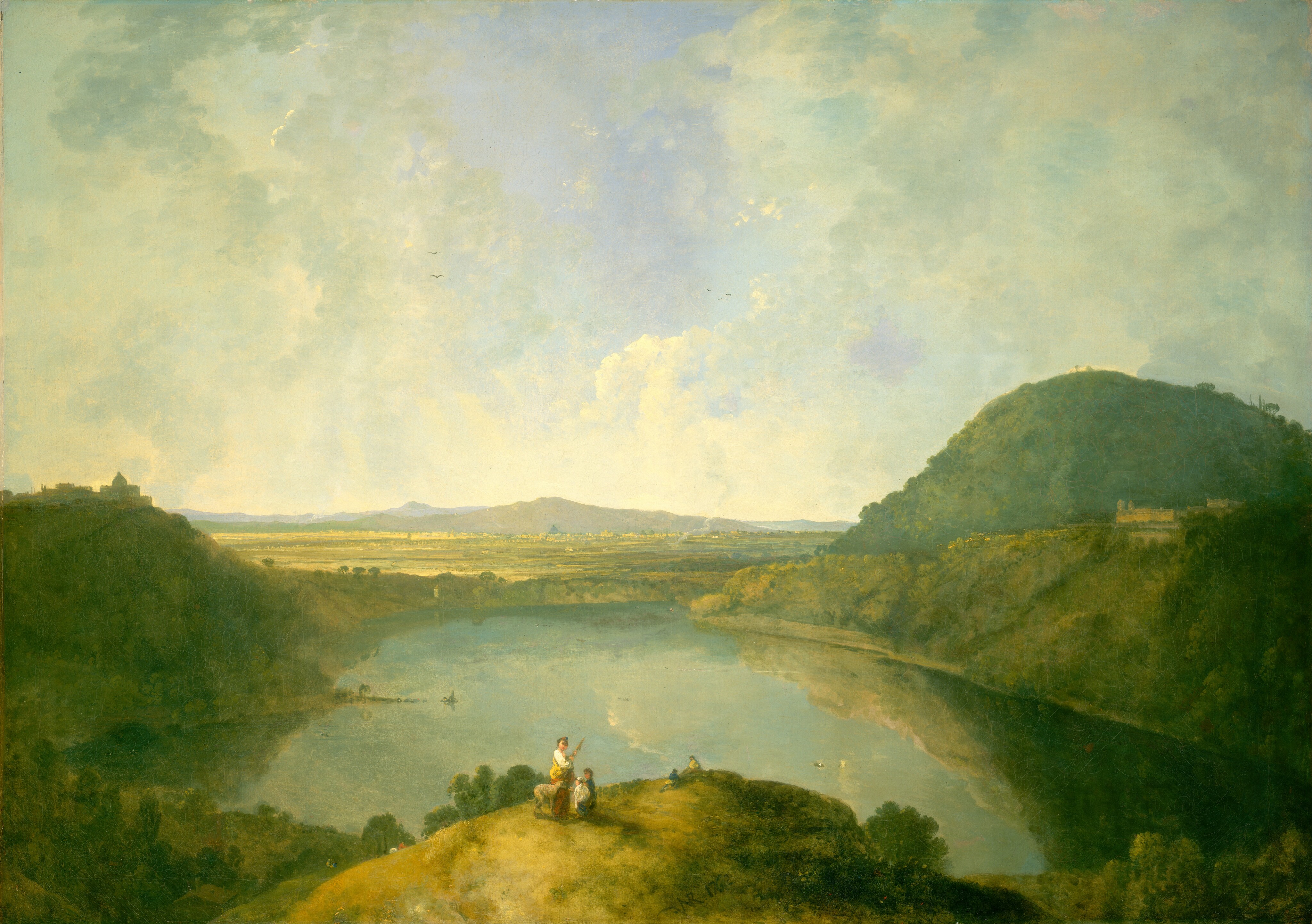 The painting shows a green landscape from an elevated point of view. At the bottom of the image, a small group of people is seen on a grassy green hill. In the closest group, there is a tall person with a dog and two children, while farther down the hill are two other small people. Behind the hill is a large, reflective body of water surrounded by trees and other hills on either side. Behind the water, the scene opens into flatlands and rolling hills under a vast blue sky with soft white clouds. There appears to be a small village far in the distance. The color palette is mostly comprised of earthy greens and warm yellows, while the sky and water are light blue.
