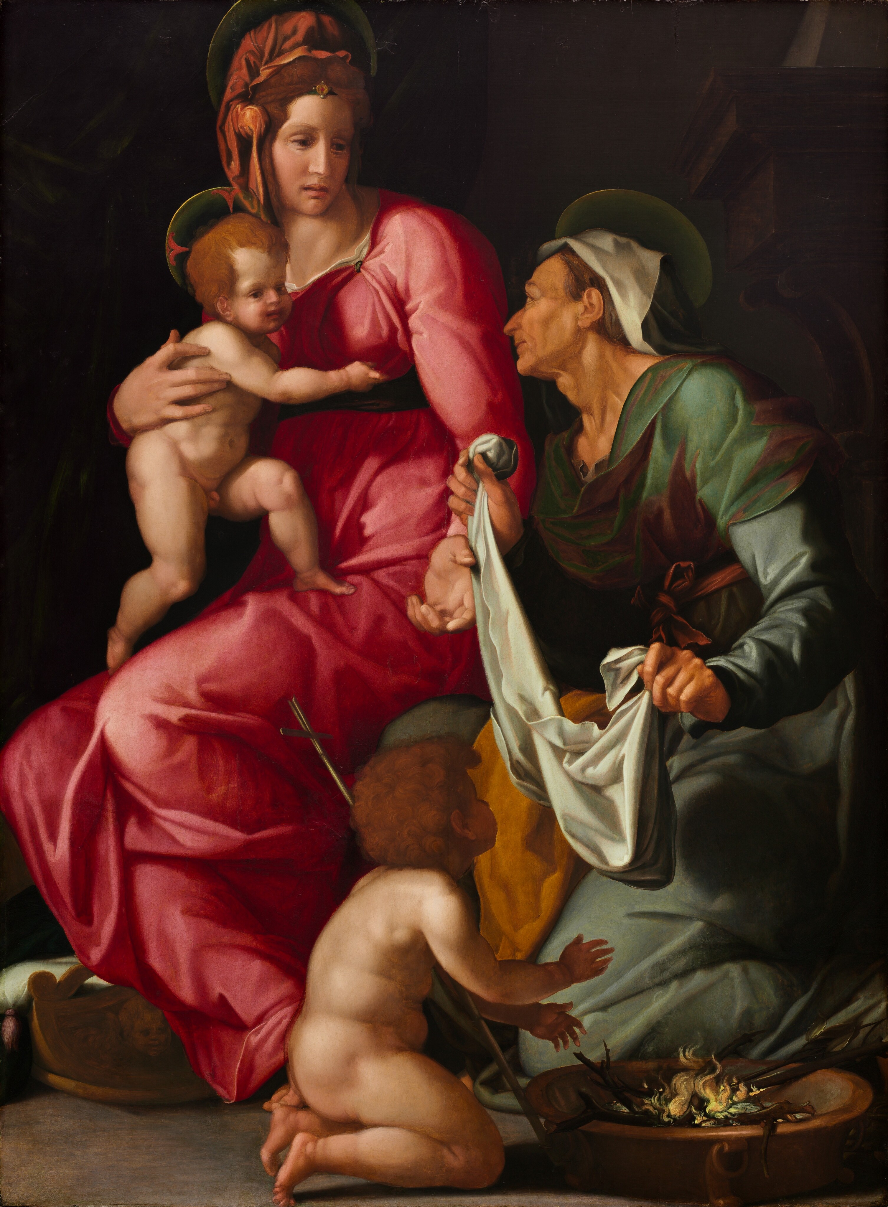 This painting shows four people: two adult women and two young children. On the left is a woman with pale skin and reddish-brown hair tied up with an orange cloth. She wears a bright pink gown that drapes over her body and is tied with a dark ribbon around her waist. She holds a nude child on her lap. The child also has light skin and reddish-brown hair. Both the woman and child have pale golden halos behind their heads, and they look to the right, towards the other woman. This woman is older, with tan skin and thin gray hair under a black and white cloth. She wears green and brown robes and holds a white cloth in her hands as she kneels and looks up at the woman in pink. She also has a golden halo around her head. In front of her is another nude child with curly brown hair who carries a thin golden cross balanced on their shoulder. This child kneels by the bottom right corner by a small fire and faces away from us. The ground is gray, and behind the women is black, with a dark column faintly visible on the right side.