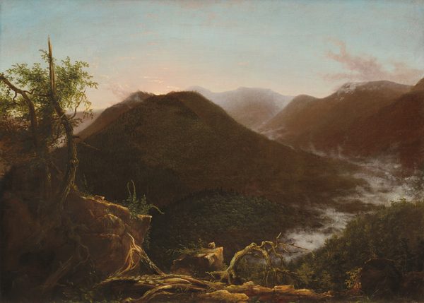 Hulking mountains are mostly backlit against a watery blue sky edged with shell pink along the horizon, which comes about two-thirds of the way up this horizontal landscape painting. Light falls across felled and gnarled trees along the bottom edge of the canvas. Two thin trunks, one of them broken to a jagged point, rise along the left edge of the composition with their green leaves outlined against the sky. The land dips steeply away into a valley wending between forested mountains. Fog has settled along the valley like a river of mist. The mountains lighten from dark, earthy green and brown close to us to muted fawn-brown in the distance. A sliver of pale-yellow sun peeks over the summit of the nearest mountain, which is to our left. Clouds kick up over the distant mountaintops, and a few wisps of peach-colored clouds float across the blue sky above. The artist signed and dated the work in black paint on a branch on the ground in the lower center, “T. Cole 1826.”