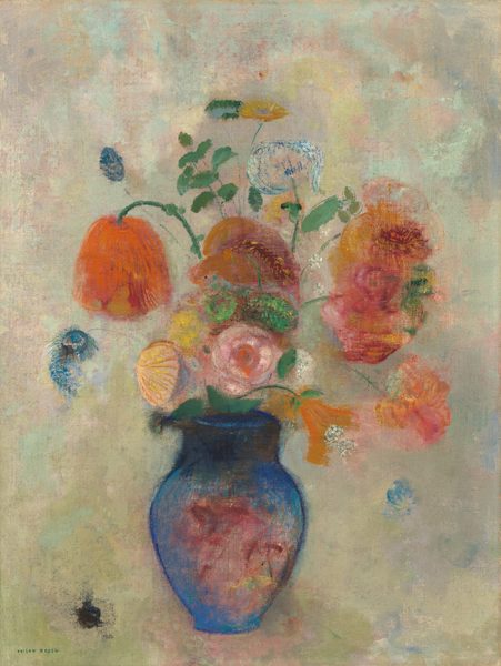 In the center of this painting is a blue vase filled with a variety of flowers in different sizes and colors. The flowers are in shades of orange, pink, yellow, and blue, with green leaves surrounding the blossoms. Some of the flowers are large and round, while others are smaller and shaped like trumpets or teardrops. At the center of the blue vase is a section of pink with some red lines. A few blue petals fall from the flowers into the air. The background behind the vase is mostly gray, although it contains mottled patches of pink, yellow, teal, and light green.