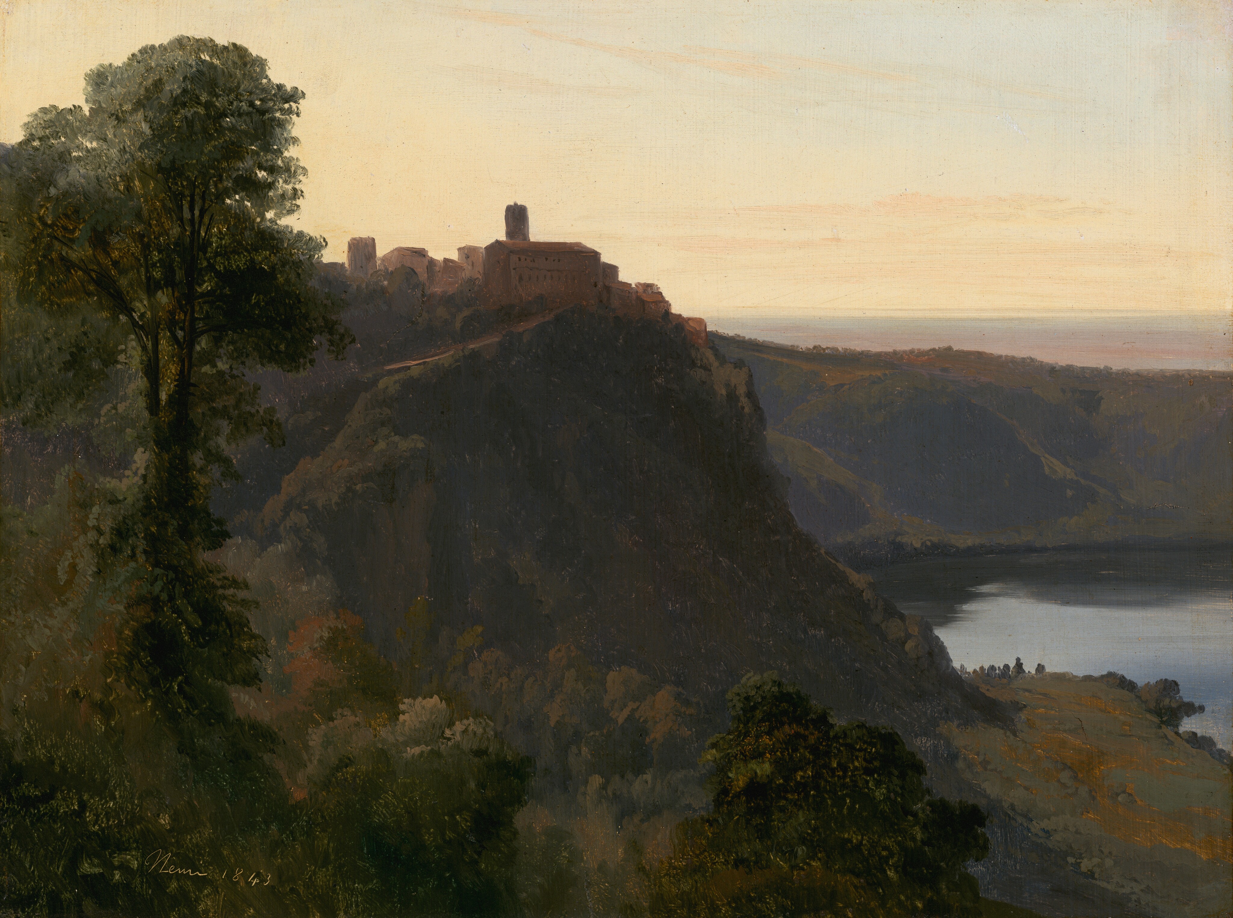 A sheer cliff looming across a deep valley is backlit by a low sunset in this is horizontal landscape painting. The tree closest to us grows up above the canopies of trees that fill the valley and nearly touches the top edge of the composition. Brown buildings clustered near the edge of the cliff are outlined against the sunset sky. Light falls across the landscape from the left, casting the right face of the cliff into shadow. The foot of the cliff angles steeply down to a paler green and gold area, and another ridge of rocky hills extends across the right half of the composition to enclose a body of still water. The horizon, which comes just over halfway up the painting, is streaked with pale rust red, lavender purple, and slate blue. The sky above is warmed to soft yellow with a few streaks of darker straw-yellow clouds. The artist signed and dated the painting in the lower left corner, “Nemi 1843.”