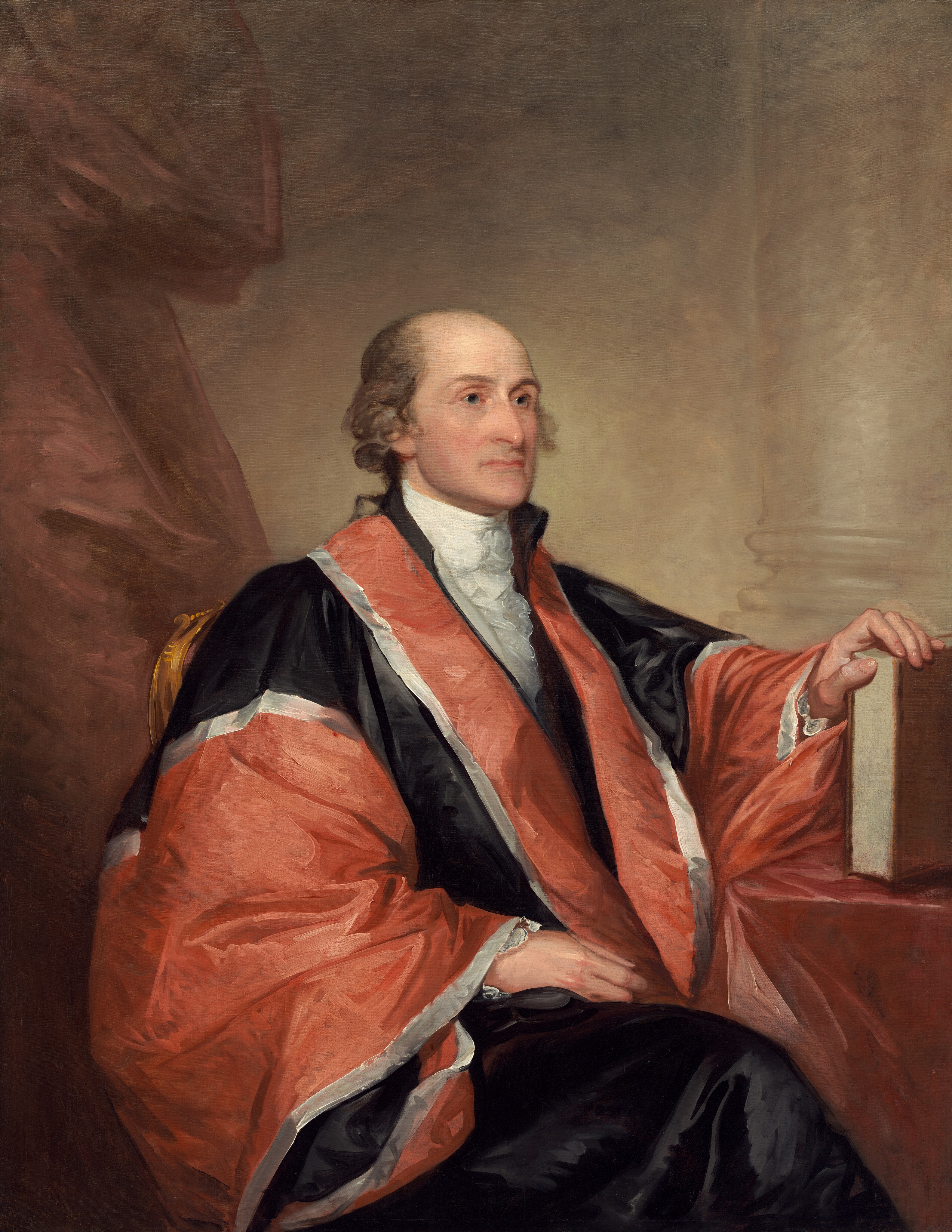 Shown from the knees up, a balding, pale-skinned man wearing a voluminous rust-red and black robe sits angled to our right in this vertical portrait painting. The man is clean-shaven, and tufts of ash-brown hair curls around his ears. He looks to our right with gray eyes under slender brows. The tip of his long nose comes to a prominent point, and his wide, thin, pale pink lips are closed. A white, ruffled ascot is tucked into the lapels of a red and black robe edged with silvery white. The fabric has a sheen, suggesting satin or silk. The man’s legs are crossed and covered with inky-black fabric. The man’s right hand, to our left, rests in his lap, and the other rests on the edge of a book propped upright on a table covered in a dusky, dark pink cloth. A muted copper-red curtain hangs to the left, and a column and its base is outlined against the parchment-brown wall behind him. The portrait is loosely painted with some visible strokes, especially in the costume and background.
