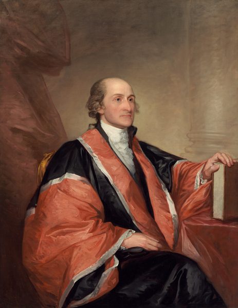 Shown from the knees up, a balding, pale-skinned man wearing a voluminous rust-red and black robe sits angled to our right in this vertical portrait painting. The man is clean-shaven, and tufts of ash-brown hair curls around his ears. He looks to our right with gray eyes under slender brows. The tip of his long nose comes to a prominent point, and his wide, thin, pale pink lips are closed. A white, ruffled ascot is tucked into the lapels of a red and black robe edged with silvery white. The fabric has a sheen, suggesting satin or silk. The man’s legs are crossed and covered with inky-black fabric. The man’s right hand, to our left, rests in his lap, and the other rests on the edge of a book propped upright on a table covered in a dusky, dark pink cloth. A muted copper-red curtain hangs to the left, and a column and its base is outlined against the parchment-brown wall behind him. The portrait is loosely painted with some visible strokes, especially in the costume and background.
