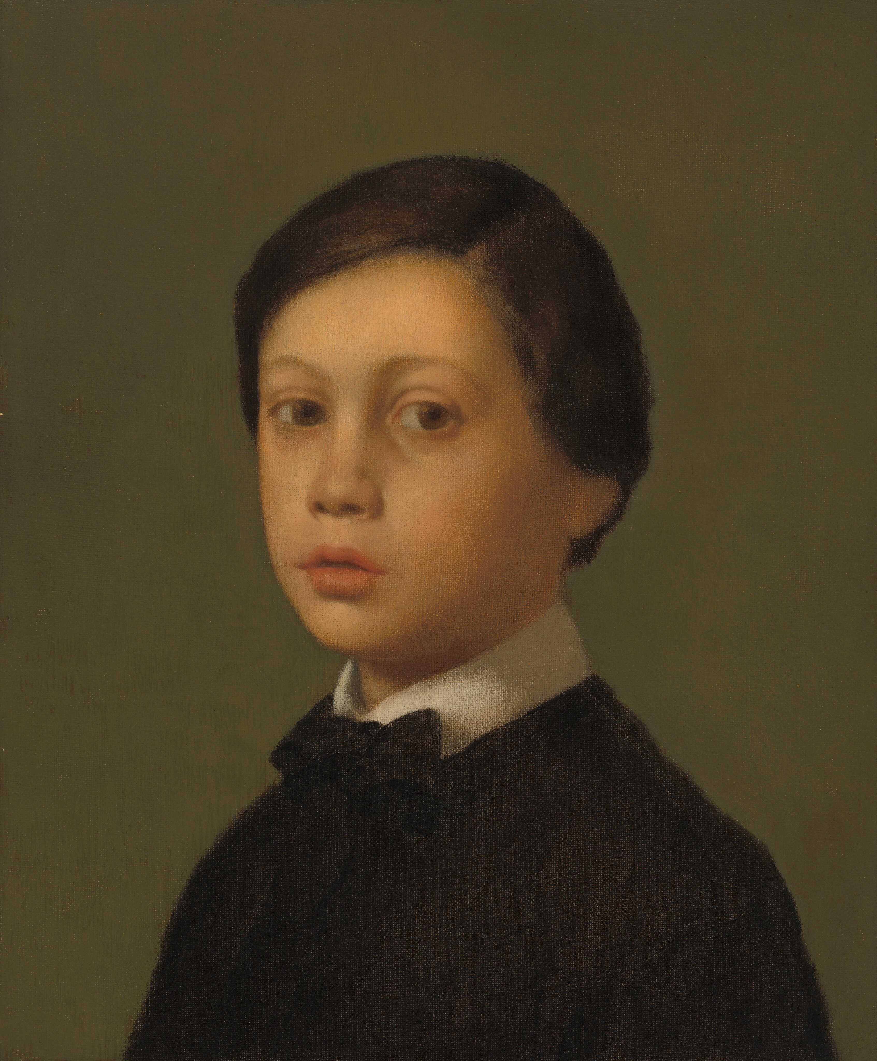 Shown from the chest up, a young, pale-skinned boy dressed in black turns to face us in this vertical portrait painting. His body is angled to our left, but he turns his head back to gaze at us from the corners of his large, hazel-brown eyes under thin arched brows. He has an upturned nose set in a round face, and his coral-red mouth is slightly open. His short dark brown hair is parted on the side and falls just below his ears. He wears a tall, oyster-white collar under a loose-fitting, black jacket tied with a black bow at the neck. The background is brownish-olive green.