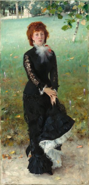 A woman with pale skin and reddish, auburn hair stands facing and looking at us on a grassy lawn, wearing a long black dress in this vertical portrait painting. She stands with her body angled slightly to our right but turns to look at us with heavy-lidded, hazel eyes under pointed brows. She has a narrow face, a straight nose, and her full, pink lips are closed. Her cheeks are lightly flushed and she has a cleft in her chin. Her copper-colored, curly hair is pulled back, and bangs sweep across her forehead. Her black dress has a fitted bodice and the long, narrow skirt ends in layers of ruffles at the hem. A spray of white fabric, perhaps taffeta, is tied in a flaring bow at her neck, partially overlapping a tomato-red object, perhaps a flower or corsage, on her left shoulder, farther from us. The tight sleeves of her dress are black lace, and the cuffs are lined with more sprays of white. She holds up her skirt with both hands, close to her left thigh. Where the hem is lifted, the layers of white fabric underneath are exposed, creating an S-shape that curves down to her feet. The sheen on the layers of ruffles suggest that the black skirt, at least, is made from silk. She wears jeweled rings on the fourth finger of each hand and dangling, sparkling earrings. She stands on an oyster-colored ground, probably a walking path, in front of a lawn that fills most of the background. Touches of yellow and pale purple suggest flowers in the lawn, which fades from muted, pine green close to us to mint green in the distance. The carpet of the lawn is broken only by a birch tree near the upper right corner. A spray of leaves, presumably from a tree just outside the composition, dips into the scene at the upper right as well. Some trees and a white, stone structure with steps and a balustrade line the top edge of the composition. The artist inscribed the work with brown script in the lower right corner, where it reads: “John S. Sargent Ronjoux 1879.”