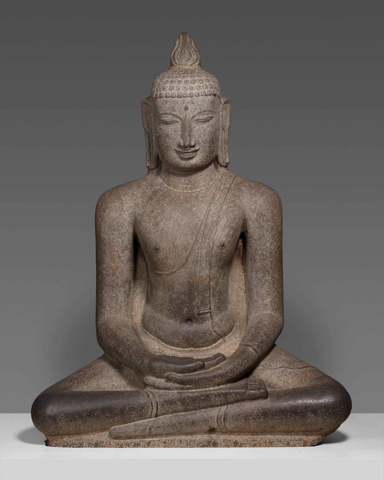 Dark stone sculpture of Buddha sitting cross-legged, hands in lap, eyes closed.