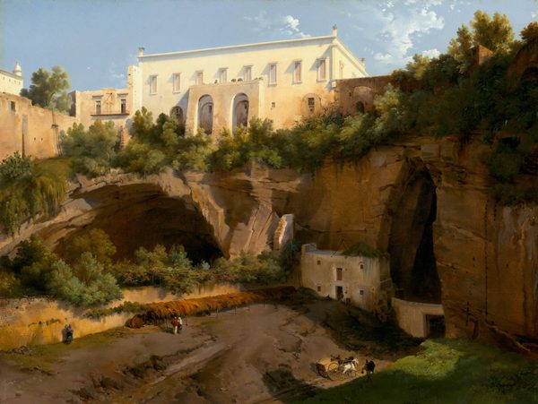 This painting shows a white and tan building on the edge of a rocky cliff, seen from slightly below. There are arched openings within the cliffside, with some other small buildings tucked into them. The ground is brown and covered with leafy greenery on the top of the cliff and in a cave on the left, with a patch of green grass in the bottom right corner. In the center, distant people and a horse-drawn cart walk on a path below the cliff, towards one of the openings. The sky above is blue with scattered white clouds.