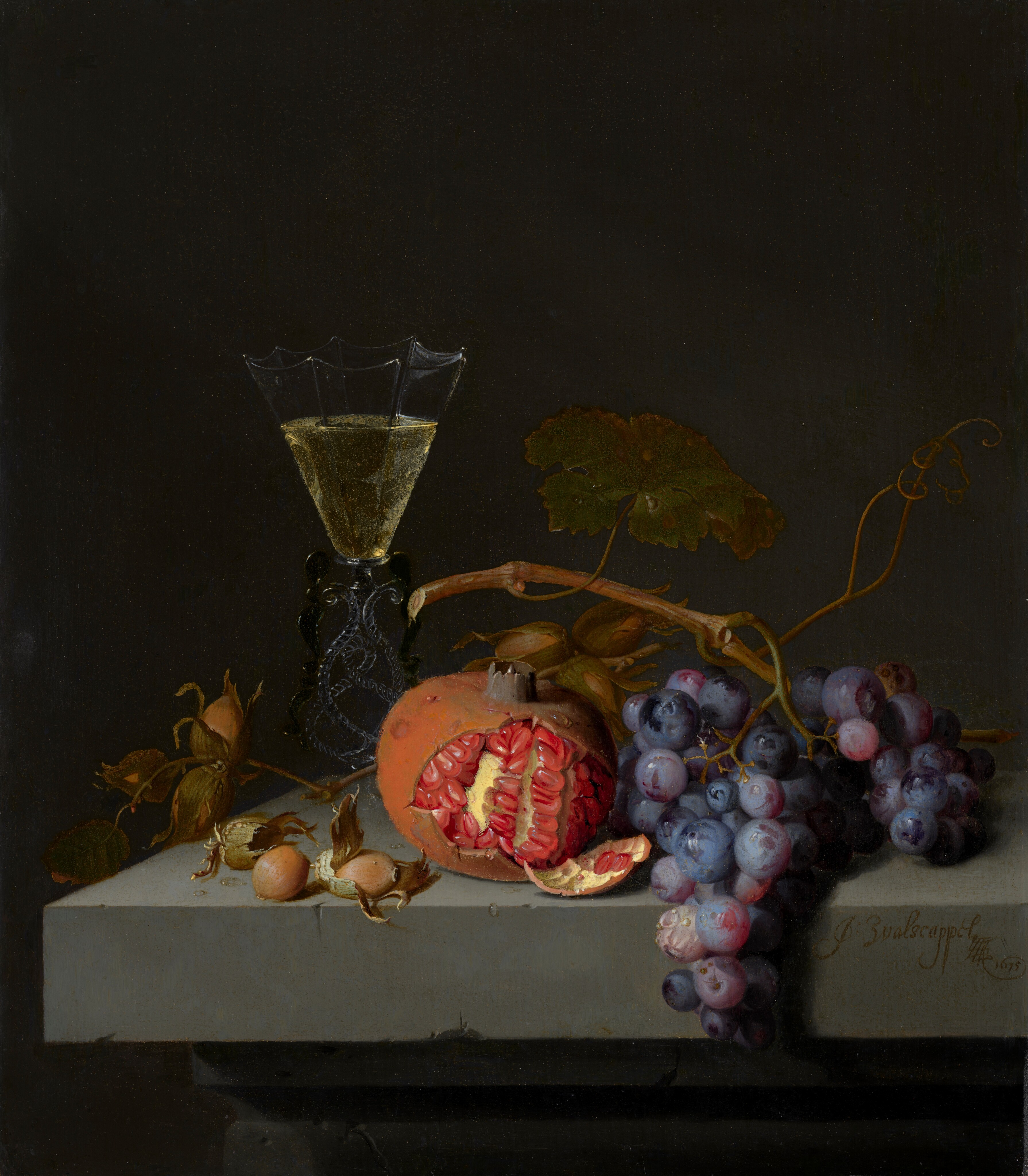 A half-peeled pomegranate, a few nuts, a bunch of purple grapes, and a glass of pale yellow wine sit on the corner of a stone ledge against a dark background in this vertical still life painting. The corner of the chipped gray ledge is close to and lines up with the lower left corner of the painting. Two hazelnuts sit near the front of the ledge, and a twig with three more nuts in papery husks are attached to a twig. Behind that, the flaring cup of the wineglass is made up of flat panels, which are inwardly scalloped along the upper edge, like an upside-down badminton shuttlecock. The stem is made of intertwining ropes of clear and black glass. At the lower center of the composition, the glistening, scarlet-red seeds of the pomegranate contrast with the rust-orange rind. Another twig of hazelnuts is between the pomegranate and the bunch of frosty purple grapes. The vine and a broad, dark green leaf arches over the grapes and pomegranate. The objects are brightly lit from our left against a charcoal-gray background. Molding under the ledge can be made out in the shadows across the bottom edge of the painting. Closer inspection reveals tiny water droplets on the stone ledge and the pomegranate. The artist signed and dated the painting in cursive text on the front face of the ledge, near the lower right corner: “J: Walscappel 1675.”