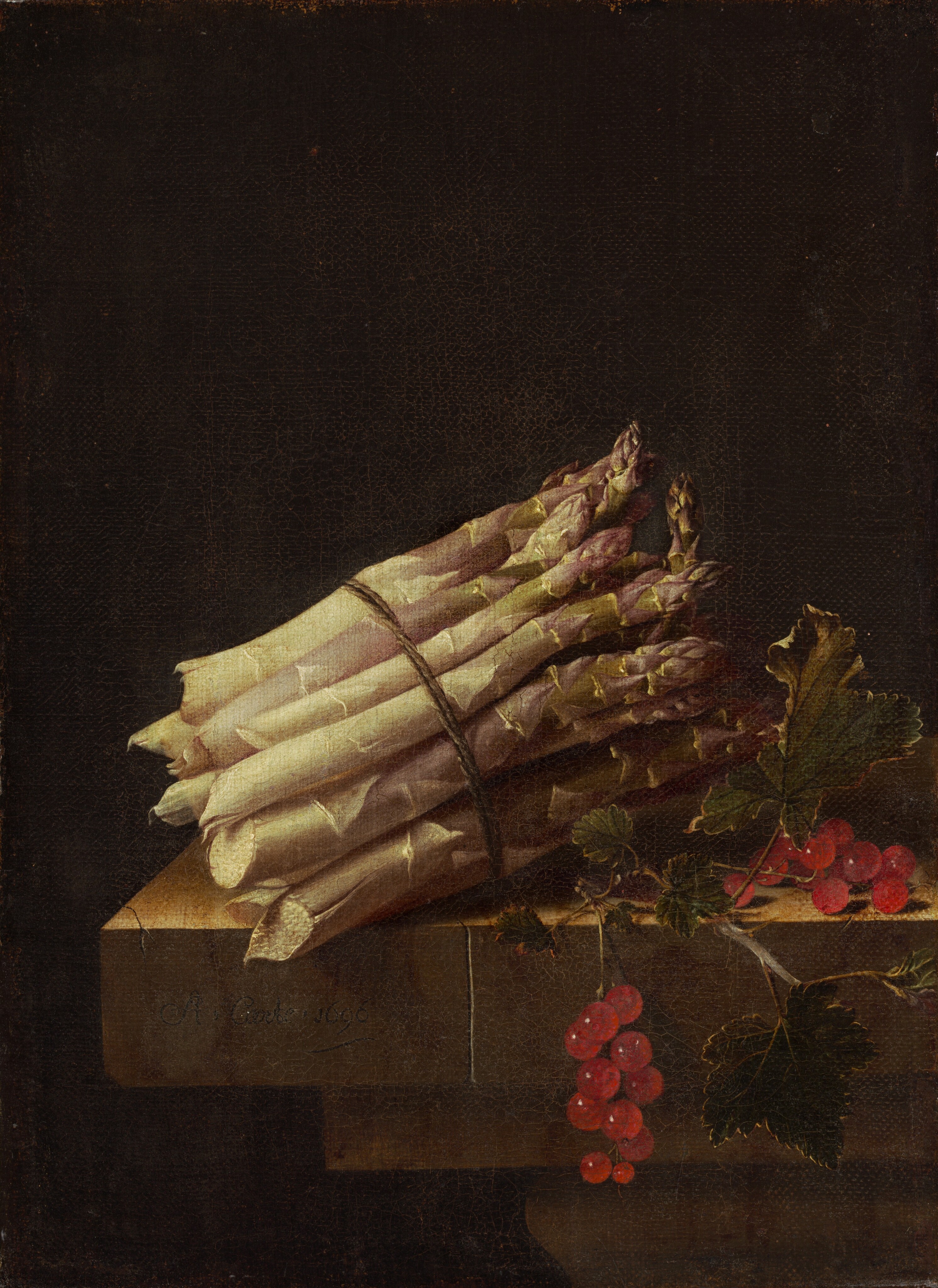 A bundle of pale green, thick asparagus stalks bound by twine and a bunch of glistening ruby-red currants sit on the edge of a stone table or ledge against a deeply shadowed background in this vertical still life painting. The asparagus is situated with the jagged, broken edges facing our left and the pointed tips angled away from us to our right. The base of the stalks are nearly cream-white, and the tips are faint green and muted purple. To our right, one the two stems of the red currant berries and leaves dangles off the front edge of the table. Light spills onto the scene from our upper left giving the currants a glassy sheen. The stone ledge or table is cracked in a couple of places. The artist signed this work as if he had inscribed his name and the date on the front surface of the table: “A. Coorte. 1696.”
