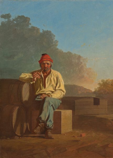 A bearded man with wrinkled, peachy skin and reddened cheeks sits and smokes a pipe on a wooden box in a landscape in this vertical painting. The man’s body faces us, and he peers at us with dark eyes under heavy, bushy white brows. Wrinkles line his forehead, the corners of his eyes, and his cheeks. He has a bulbous nose and a gray beard, and the long-stem pipe is pinched in his downturned mouth. His shaggy gray hair is covered by a cardinal-red cap. He wears a blousy daffodil-yellow shirt, which is loose around the neck, faded and patched blue pants, and scuffed brown boots. His legs are crossed with one knee over the other, and one fist rests in his lap. The other elbow is propped on a pyramid of three wooden barrels stacked on their sides to our left. A few bits of bricks or red stones are near the man’s feet, and a wooden houseboat with a low-pitched roof is in the near distance, to our right. The platform under the structure floats on a river, which is lined with trees to our right and mountains to our left. The sunset warms the face of the mountains and the trees to red and gold. Sage-green and peach clouds billow above the man, dividing the sky diagonally in front of bright blue sky beyond. The artist signed and dated the painting in the lower left corner, “G.C. Bingham 1850.”