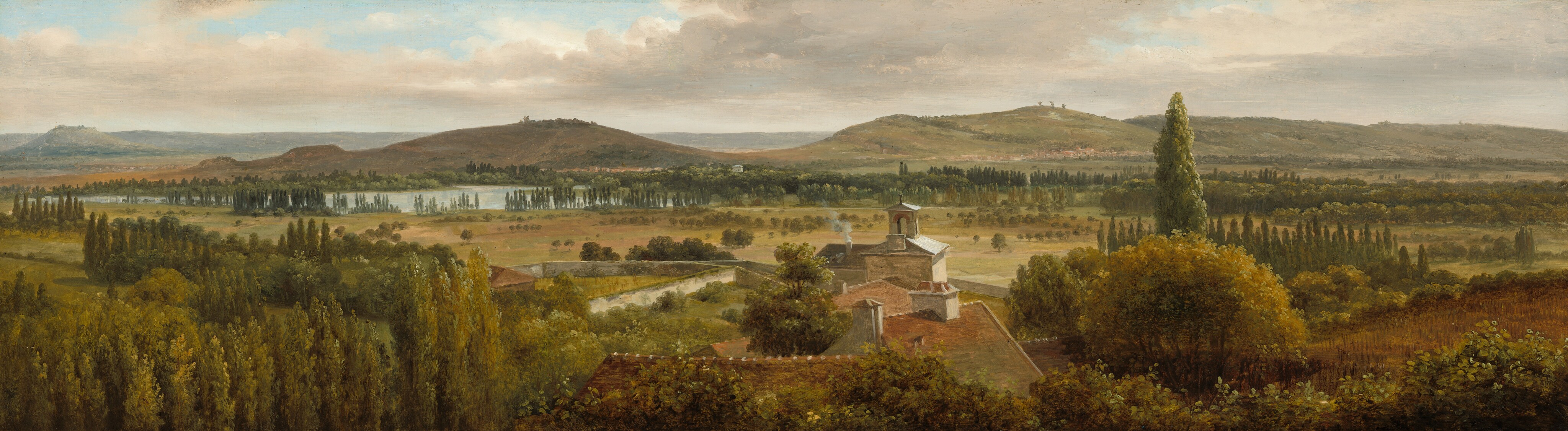 We look across the tops of trees down onto the roofs of a cluster of buildings and then a grassy expanse, a body of water, and rolling hills in this notably wide landscape painting. The trees are painted with shades of pine and olive green. At the center of the composition, the roofs are muted terracotta red with white chimneys except for the farthest structure, which has a gray roof around a lantern, perhaps indicating a church. Smoke puffs out of one chimney there. Trees with round canopies dot the pale, grassy field beyond that, which leads back to rows of tall, dark green cypress trees. A ribbon of ice blue across the left third of the painting indicates a body of water before russet-brown and muted sage-green hills roll into the deep, hazy distance. The horizon comes about two-thirds of the way up the painting, and glimpses of pale blue sky are visible through breaks in a blanket of pale gray and cream-white clouds above.