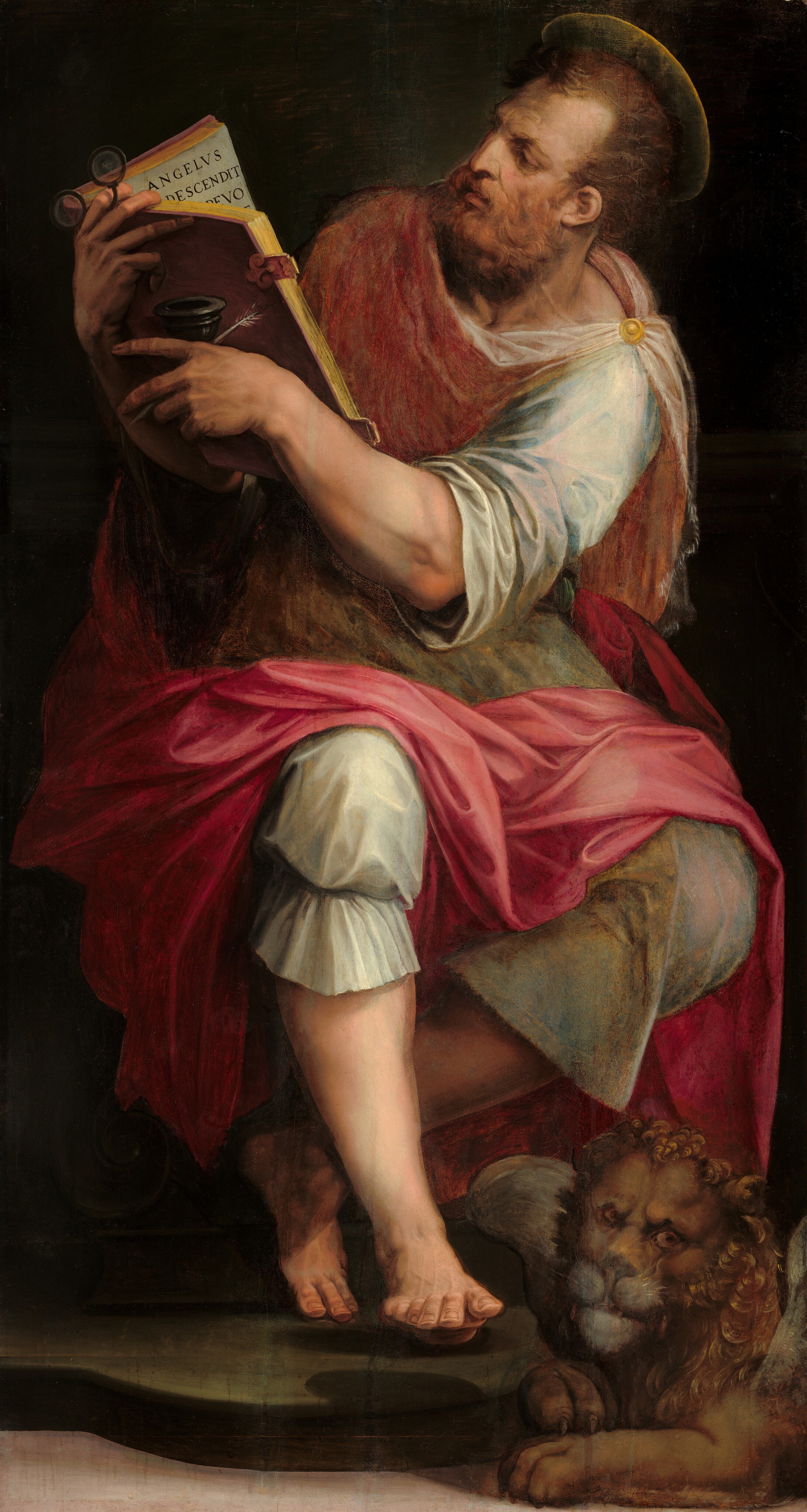 A pale-skinned, muscular man sitting and reading a book as a lion rests at his feet fills this vertical painting. The man’s knees are angled slightly to our right but his torso twists back to the left. His head follows that direction so he’s almost in profile as he looks at the book, which he holds up to our left. His brows are deeply furrowed, and he has a bumped, blade-like nose. He has short, copper-red hair and a squared beard. He wears a tunic and knee-lengths pants that shimmer in shades of topaz blue and pearly white under a carnation-pink cloak that drapes from his shoulders and across his thighs. A round, gold pin holds the cloth in place on his left shoulder, to our right. His lower legs and feet are bare. He rests the heel of one foot on a rounded plinth and lifts the toes so they come at us. The other knee bends deeply and the toes of that foot perch lightly behind the first leg. The man leans to our right to look at the open book, which he holds in both arms to the left. Visible text on the far page reads, “ANGELVS DESCENDIT EVO.” He braces a black inkpot and spindly white feather quill in one hand and holds a pair of pince-nez glasses with the other. The lion is small in comparison to the man and has a curly mane and translucent gray wings. The background is dark except a strip off-white floor along the bottom edge.