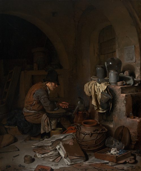A light-skinned man sitting near an oven is surrounded by papers and vessels, all within a shadowy room in this vertical painting. The scene is dominated by chocolate and clay brown, black, slate blue, and shades of gray. The man sits facing our right in profile near the center of the painting. He wears a tall black cap that shadows his eyes and a rust-brown sleeveless garment like a vest over dark, steel-gray, long sleeves. Cream-white fabric tied around his waist could be an apron, and more white fabric drapes over his knees. Brown hair is visible behind his ear, he has a mustache, and his lips are parted as he looks down toward the instruments in front of him. He is hunched over, the elbow closer to us on what might be a flattened bellows, and he holds tongs in his left hand. The vessel in front of him could be made from pewter or glass, and it has a high, curved top and a long spout angled downward. Other pots and a red cloth are jumbled with large, leather-covered folios like thick folders of papers on the floor close to us. More papers, pots, and containers sit on a wide ledge over the open fireplace or oven to our right. A piece of parchment-white cloth hangs down the front of the oven next to a leather knapsack that hangs from the mantle. The top zone of the painting is deep in shadow but there seems to be an arched window or door covered with a wooden shutter to our right, behind the oven. A piece of paper affixed to the wall near the opening shows a vessel like the long-spouted vessel in front of the man. A shallow wooden box near the lower right corner seems to be filled with crumpled paper or cloth. The artist signed and dated the front face of the box with light letters: “C. Bega Ao. 1663.”