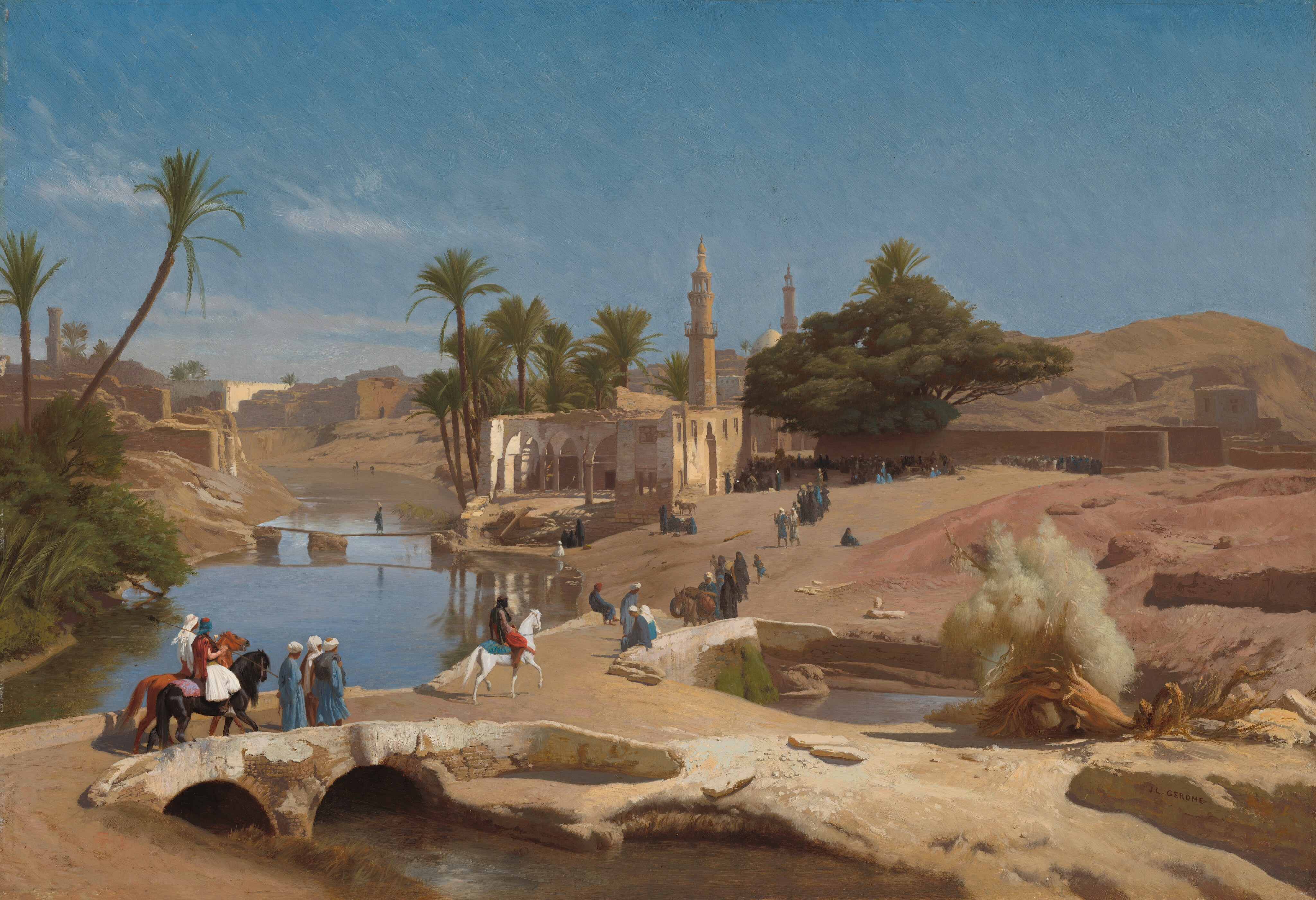About a dozen people walk and a few ride horses across a bridge spanning river that cuts through a sandy landscape in this horizontal painting. A few wisps of clouds drift across a vivid blue sky over the horizon, which comes halfway up the composition. The waterway winds from the lower left corner into the distance parallel to the left edge of the painting. A bank of shrubs and two tall palms lean toward the water from the left bank, and brown and cream-white buildings line both sides of the water to the horizon. People sit on the low wall of the bridge in the lower left corner, and a person leads a donkey laden with sacks toward us on the far side of the deck. The bridge is shaped like a capital T laid down, so the top crossbeam spans the river. The lower branch divides the river on our side of the bridge. Some rocks and a gnarled trunk lie across this strip of land. Farther up the river and to our left, a single person walks across a second bridge made up of planks supported by rocky pilings. That bridge meets the far bank near the remains of a building with pointed arches and a tower-like minaret. Verdant green canopies of a cluster of palm trees flare over this building. People who walk and ride across the bridge create a loose line that extends to a larger gathering beyond the building. The group gathers in the dense shade of a wide-canopied tree, which grows high over a brown wall. More rooflines, including a dome and another minaret, stack along the horizon beyond the tree. The people wear robes and turbans in bright white, aquamarine blue, brick red, and black. The artist signed the painting as if he had written his name on the face of a rock in the lower right corner, “JL GEROME.”