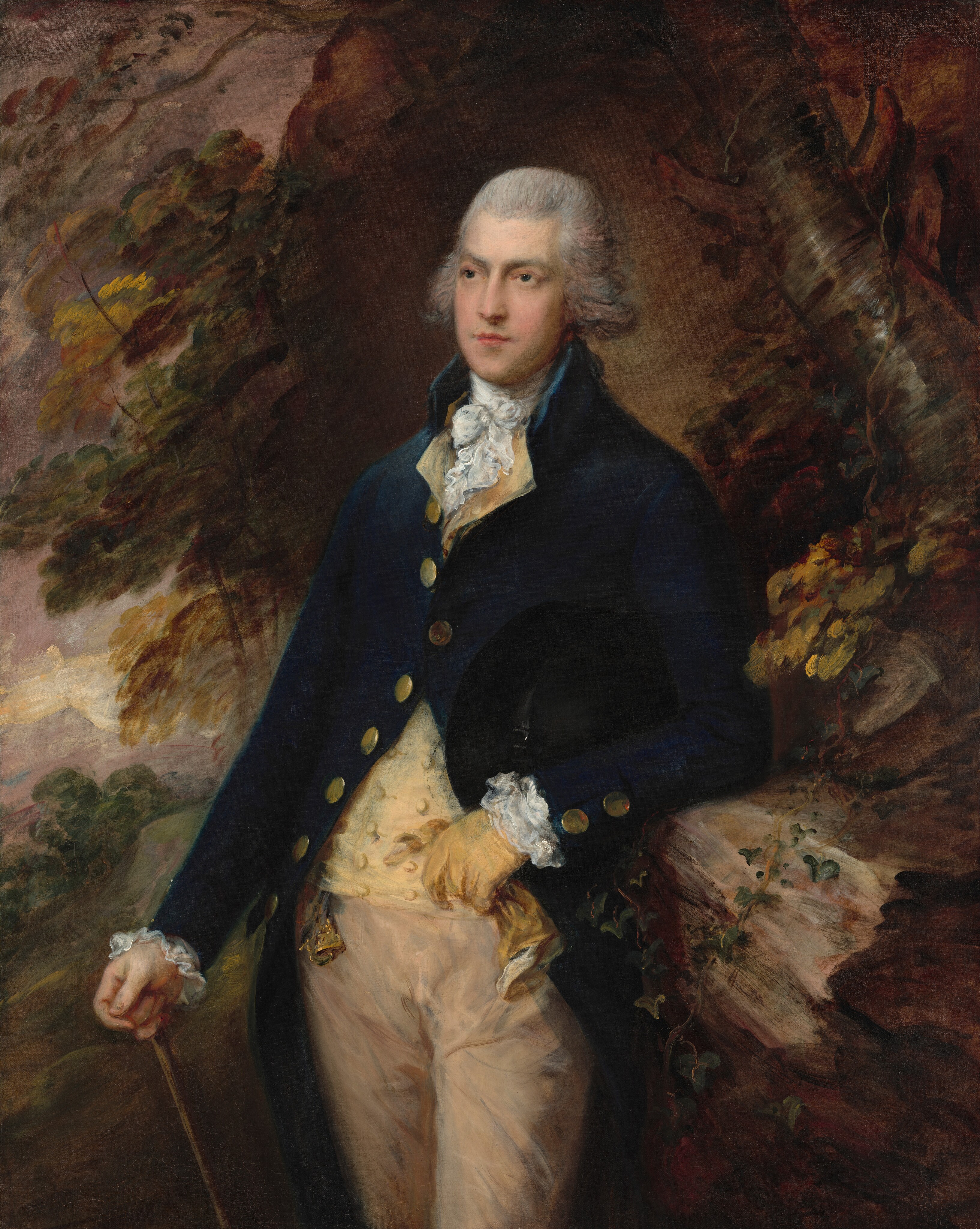 This painting is a portrait of a man standing, seen from the knees up, his torso and head slightly turned to the left. The man has pale skin and gray hair styled back from his face and forming curls around his ears, and he has a sharp nose, thick gray eyebrows, and pink lips set in a neutral expression. He wears a dark blue coat with gold buttons, a pale-yellow waistcoat, and a frilly white cravat at his neck, with more white frills at his cuffs. His trousers are tan. His left arm is bent, resting on a tall rock formation on the right. His left hand is gloved and holds the other yellow glove. His bare right hand holds a thin brown cane. The background features loose leaf shapes in warm autumnal colors, with the gray-brown trunk of a tree visible in the top left and glimpses of a purple and gray sky on the left side. The area behind his head is brown.