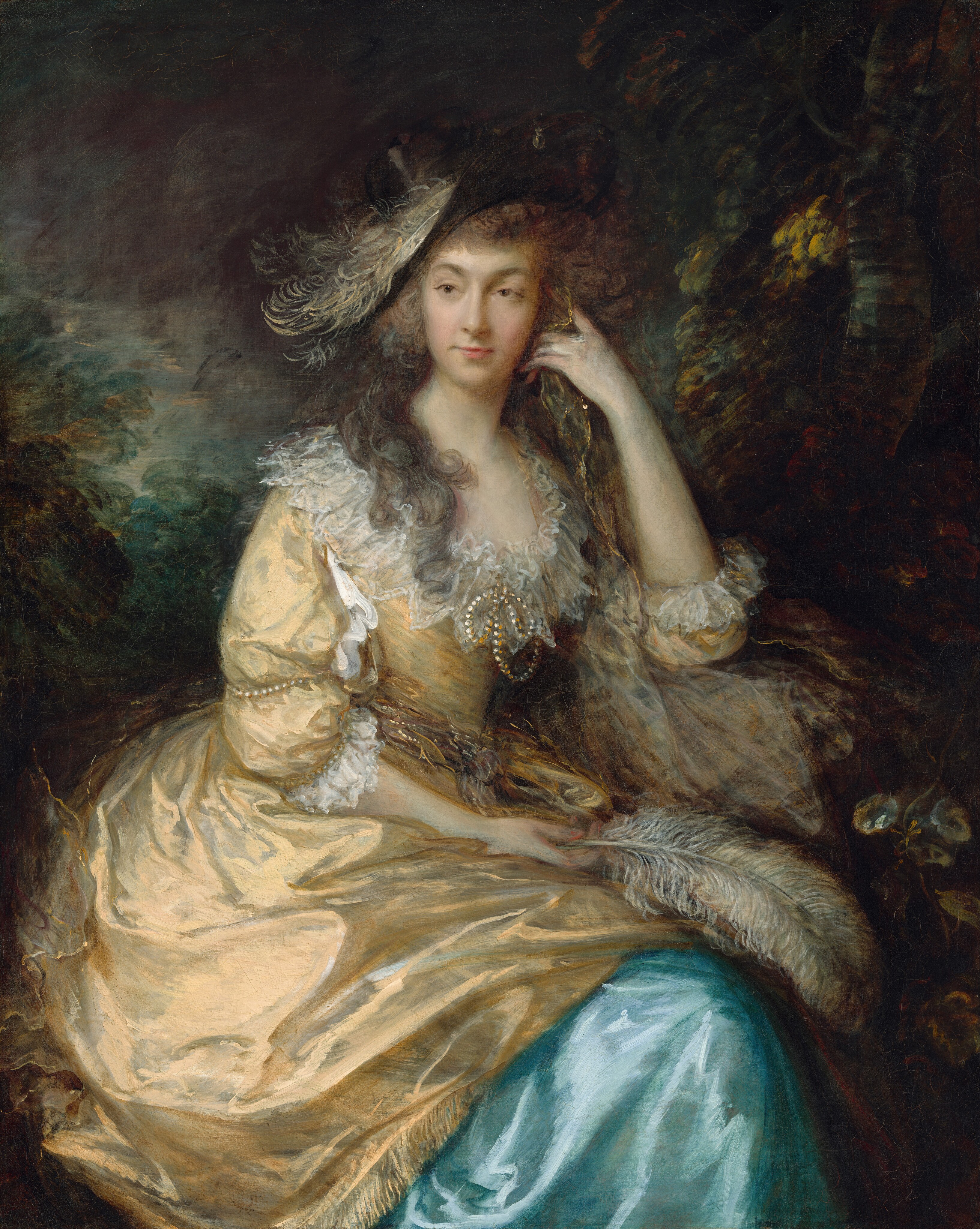 Shown from the knees up, a woman sits looking off into the distance in front of a deep, shadowy landscape in this vertical portrait painting. The woman’s body is angled slightly to our right, but she turns her oval face to the left to gaze off with brown eyes. Her upper lip is thin, and her lower lip is fuller. A cloud of ash-brown curls frames her face, and long locks fall over her shoulders. Her wide-brimmed black hat is set at a steep angle to our left. The hat has a white feather lying along the front edge and a pearl hanging from the top front of the brim. Her butter-yellow gown has translucent white ruffles along the low, scooped neckline and a strand of pearls tied at in a bow at the front of the chest. The puffy sleeves come just past the elbows and are similarly lined with ruffles and encircled with pearls. The overskirt drapes over a topaz-blue underskirt. The woman holds a feather in the hand resting in her lap. Her left elbow, to our right, is propped on a stone and that hand holds a gold-colored scarf up by her face. Deeply shaded trees and a murky blue sky fill the background. The portrait is loosely painted in the clothing and background.