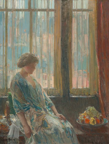 Shown from the knees up, a woman wearing an ice- and teal-blue dress and shawl sits in front of a window in this vertical painting. The scene is painted loosely with brushstrokes especially evident in the clothing and background. The woman takes up the bottom left quadrant of the composition. Her knees are angled to our right, and she looks down in that direction. She is lit from our left so her face falls into shadow, but her profile is outlined against the sheer curtains hanging behind her. Her head bows slightly, and she has rosy cheeks, a rounded nose, and her lips are closed. Her brown hair is pulled loosely back and up.  Her arms lie limp, one in her lap and the other, closer to us, alongside her body. A jewel-toned blue shawl is wrapped around her shoulders over a paler, long dress. The woman sits back in a window seat or bench against a leaf-green cushion. A turquoise-blue dish on the bench to our right is piled high with yellow and red fruit and glassy green grapes. Along the left edge of the canvas, next to the woman, white streaks suggest a cloth next to a form with honey-yellow specks painted on a bronze-orange shape, perhaps a basket. Translucent yellow curtains hang across the windows, which fill the top two-thirds of the canvas. Shapes painted in shades of smoky blue and peach outside suggest buildings and skyscrapers. A russet-red curtain is pulled to the right. The artist signed and dated the lower left corner, “Childe Hassam 1912.”