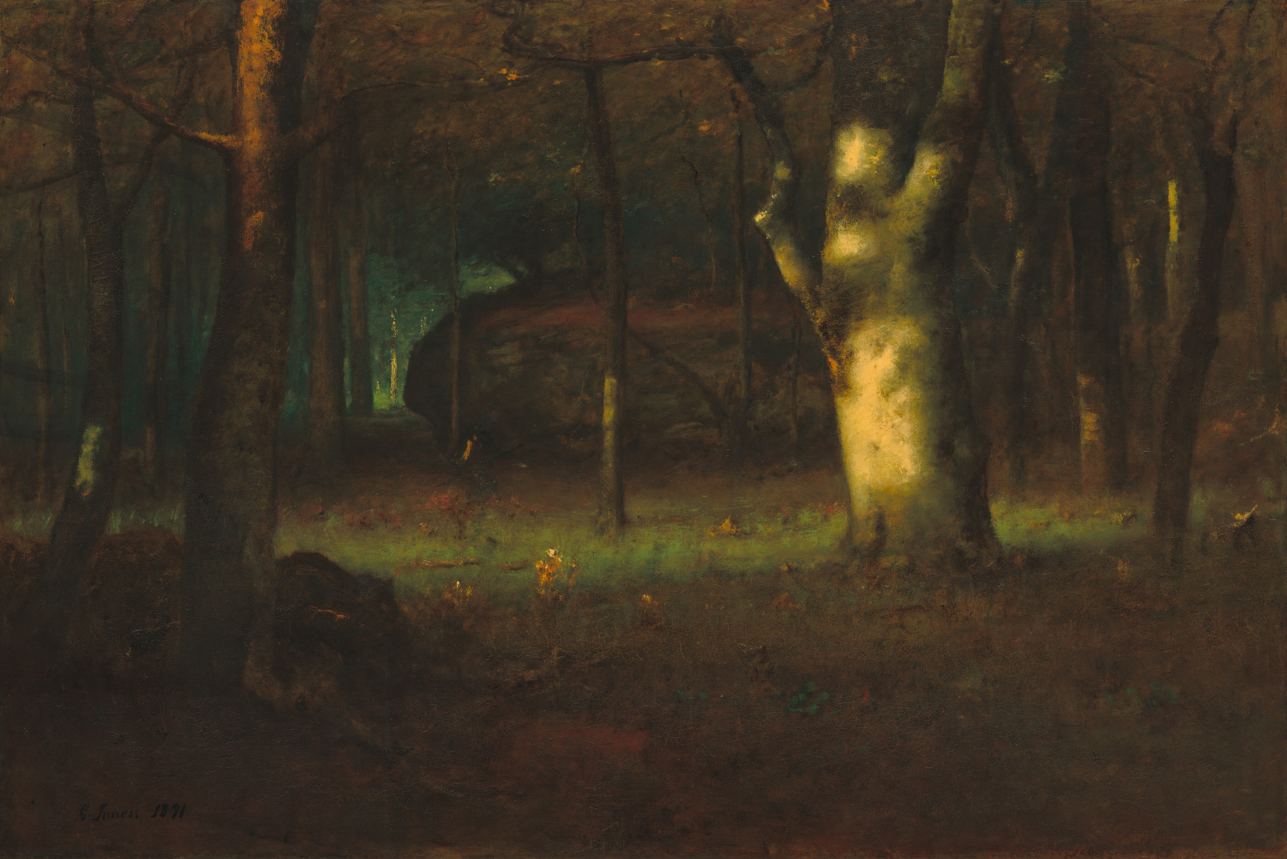 A shaft of warm light from our left pierces a dark wood filled with tall trees in this horizontal landscape painting. The light falls on a stout white trunk and a portion of the moss-green forest floor near the center of the composition. The trunk is covered with patches of olive green and brown, while the other trees have high canopies of burnt-orange leaves, which reach off the top and side edges of the canvas. The ground is carpeted with growth painted in warm tones of brown and touches of scarlet red and pine green. A gray and brown boulder with a slash of rust orange near the center of the painting lies nestled among the trees beyond the white trunk. A lighter, emerald-green area glows to the left, in the distance beyond the boulder. The artist signed and dated the lower left, “G. Inness 1891.”