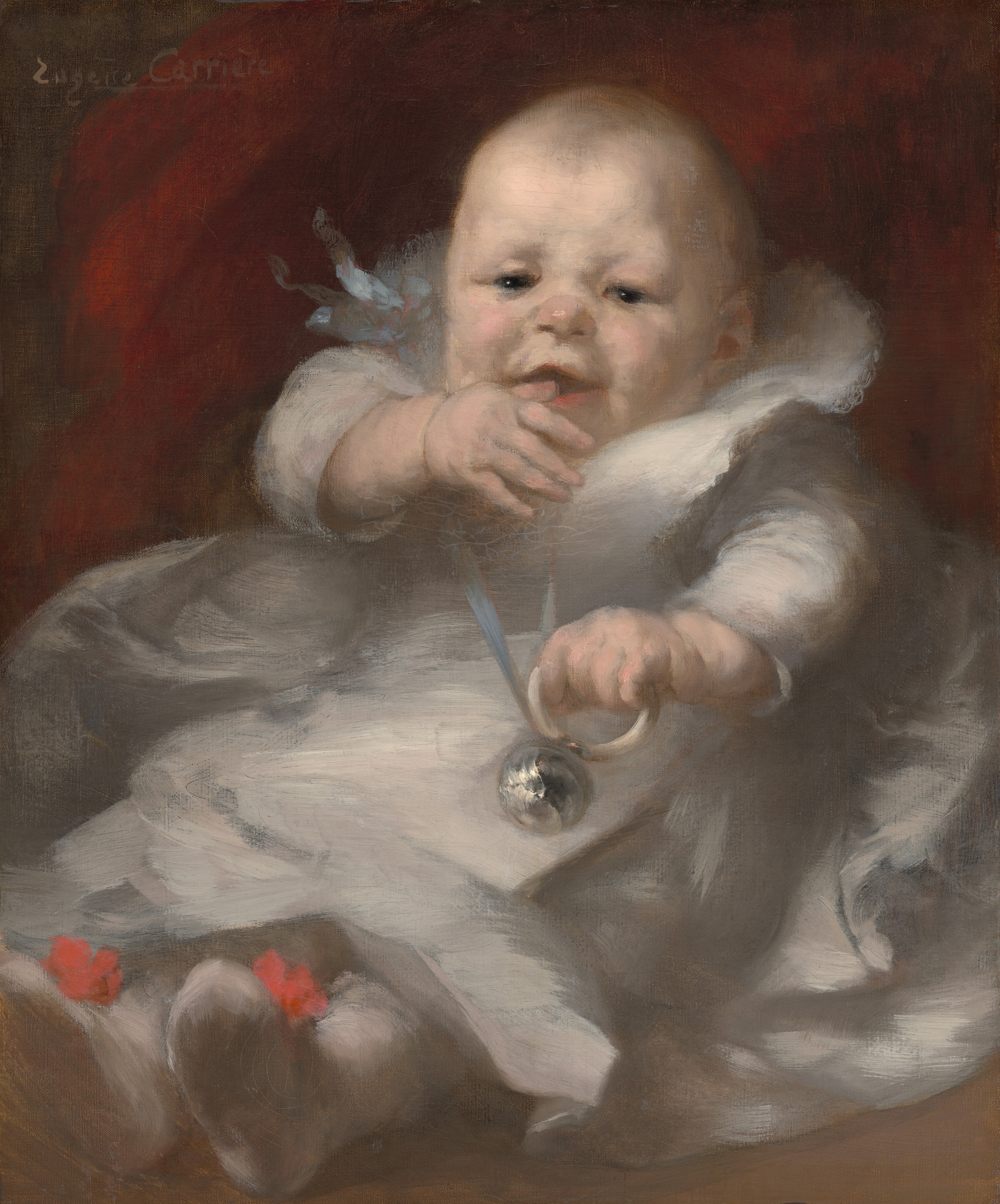 This image shows a young baby from head to toe. The baby is upright, possibly seated or reclined, with soft, rounded features, rosy cheeks, small eyes, and a slight smile. The hair is sparse and light-colored. The baby is dressed in a light-colored garment with red accents on the feet, likely the tops of booties or socks. The baby is holding a silver object attached to a ribbon or string in one hand, possibly a rattle. The background is dark with some red tones, offering a contrast with the light clothing. The artist's name, "Eugène Carrière," is visible in the upper left corner as a signature.