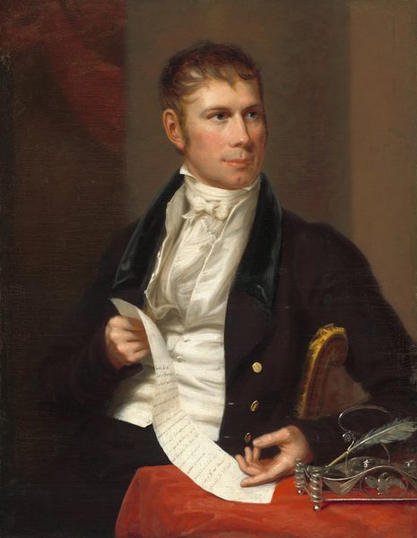 This painting shows a man seated behind a table, his torso facing us and his head slightly turned to the right. He has a fair complexion, a strong brow, and pink lips in a slight smile. His short brown hair falls across his forehead in loose waves. He is dressed in a black coat with gold buttons over a white vest and a high-necked white cravat. His right hand is holding a long piece of paper with lines of writing on it. The end of the paper rests on the table in front of him. His left hand is also on the table, pointing to the paper. The table is covered with red cloth, and on it is a silver inkwell and a feather quill. The background is in shades of brown, with a hint of red near the upper left corner, perhaps suggesting draped fabric.