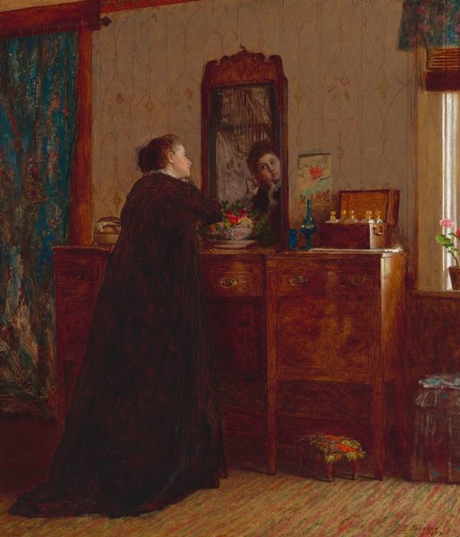 This painting shows a woman standing in front of a wooden dresser with a mirror, her back to us. We can see her face reflected in the mirror. She is gazing at her reflection with both of her hands lifted towards her slightly tilted face. The woman has pale skin and dark hair neatly styled away from her face, and she is wearing a dark gown with white ruffles around the neck. On the dresser, there is a floral arrangement, a pair of blue bottles, and a wooden box holding more containers. Behind the dresser, the background includes patterned wallpaper, a blue curtain on the left, and sunlight coming through a window on the right. The floor appears to be covered by a patterned rug.