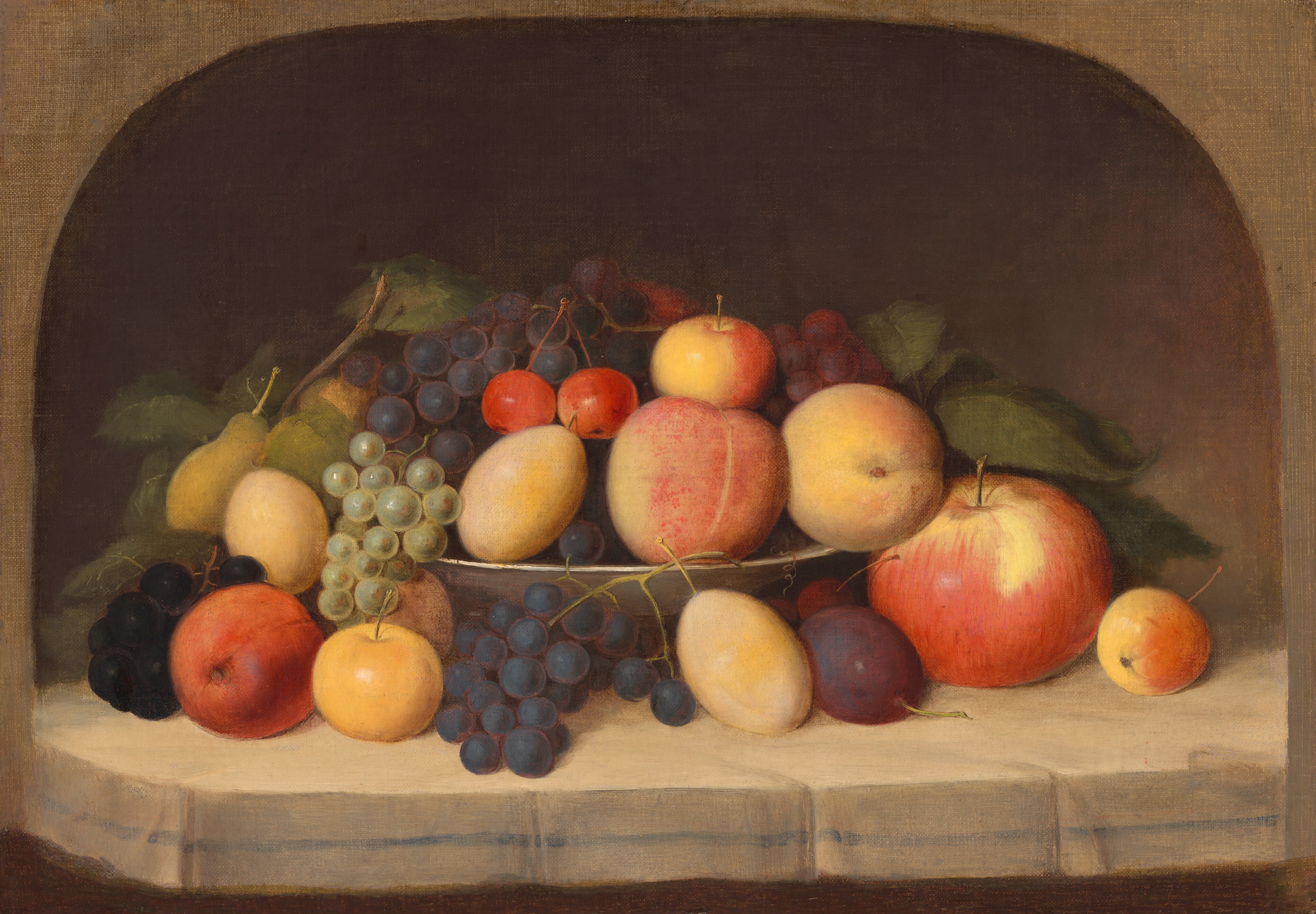 This painting shows various pieces of fruit arranged in a thin white bowl, including apples, peaches, green and purple grapes, cherries, pears, and plums. Some of the fruit is overflowing from the bowl, and rests on the white surface below, surrounding the bowl. Many of the pieces of fruit have thin stems attached to them, and some have thick green leaves. Behind the fruit, the background is dark brown, and there is a tan arched border around the painting.
