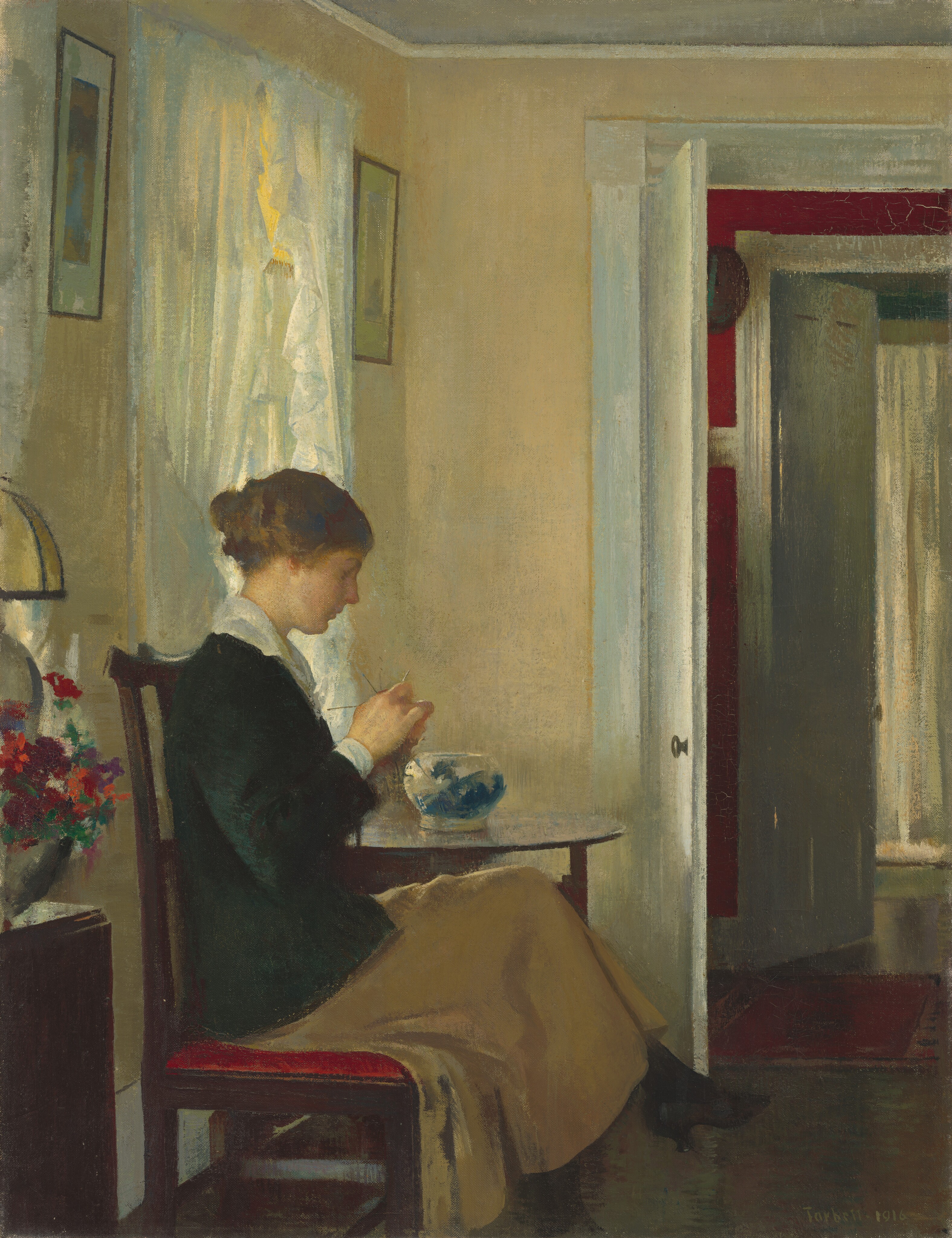 This painting shows a woman seated on a wooden chair, facing the right with her head slightly tilted down. She is focused on the thin silver needles she holds in her hands. She has light skin and brown hair put up into a bun, and she wears a dark green long-sleeved top with a white collar, a long tan skirt, and black shoes with short heels. On the round table next to her, there is a bowl decorated with white and blue patterns. On the left, a tall brown surface is partially visible, with a vase of red, orange, and purple flowers on top of it. The room has pale-yellow walls, and there is an open window with sheer curtains behind the woman. Framed artwork is on either side of the window, near the gray ceiling, and on the right is an open white door leading into another room with red walls and another open door.