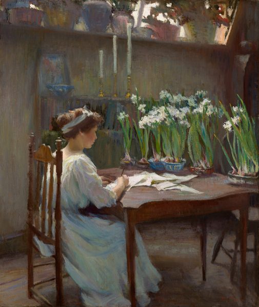 This painting shows a woman in profile, sitting at a wooden table strewn with papers, her body angled away from us. She has pale skin and rosy cheeks, and her light brown hair is tied up and adorned with a light blue headband. She wears a light-colored gown that appears mostly white, but also has streaks of light pink, yellow, pale green, and light blue. She is writing on one of the sheets of paper that is scattered on the table. Six potted plants with long green stems and white flowers line the edge of the table across from her. She sits in a room with a brownish-gray wooden floor and pale green walls. There is a bookshelf to the left of the woman, with a framed photograph, a small bowl, and three long white candlesticks of varying heights on top of it. Above the bookshelf is a tall window ledge which is also lined with leafy plants in pink, yellow, light blue, and white pots. White light shines in from between the plants, casting a bright glow on the back of the woman and faint shadows below the table and the chair she sits on. The brushstrokes of the painting, especially those in the background, are visible, giving the painting a slightly hazy quality.